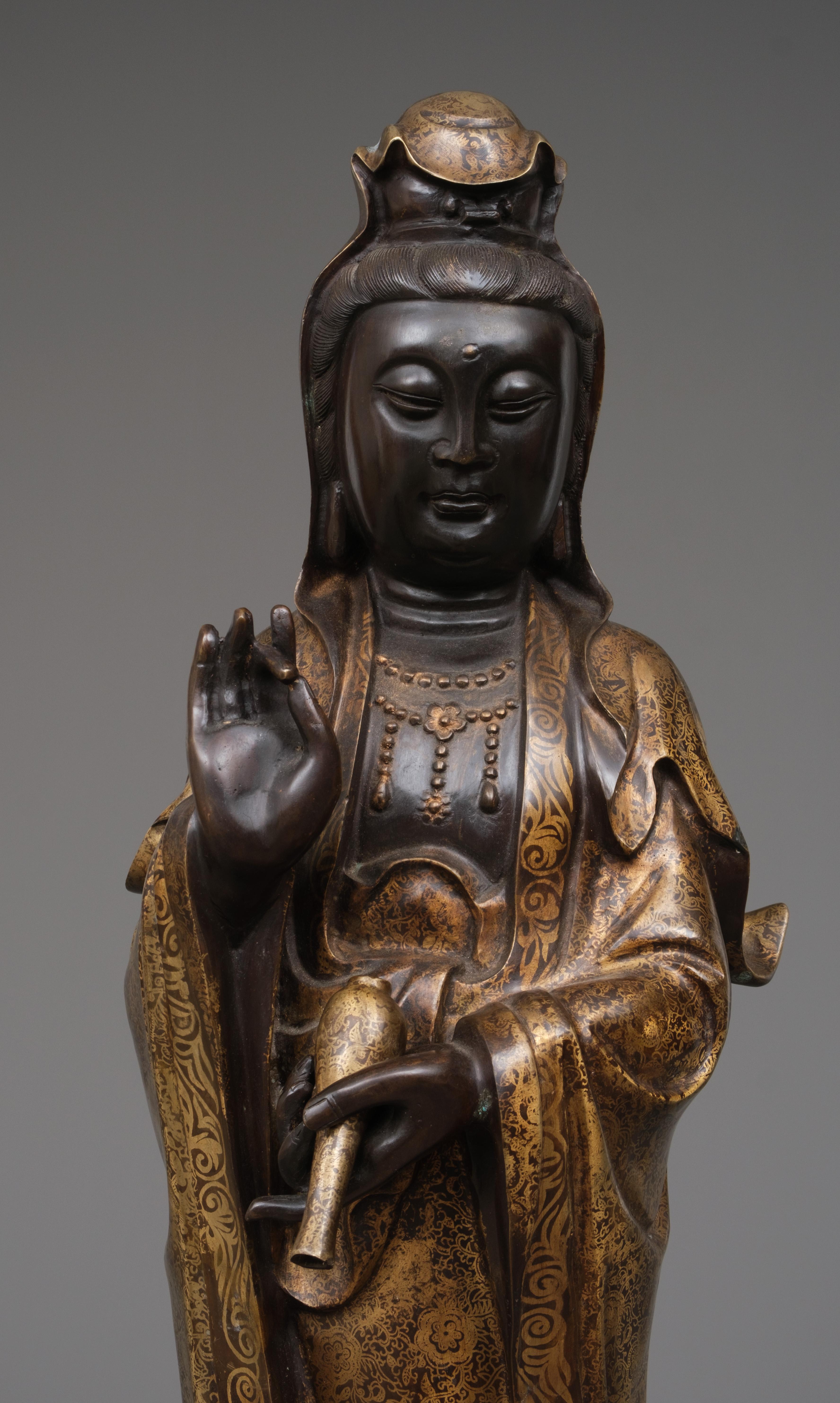 Impressive, capital Chinese bronze figure of a standing bodhisattva Guanyin, revered as the Goddess of Mercy, also recognized as Avalokiteshvara or Kannon. The figure is masterfully crafted as a single piece from dark brown patinated bronze, with