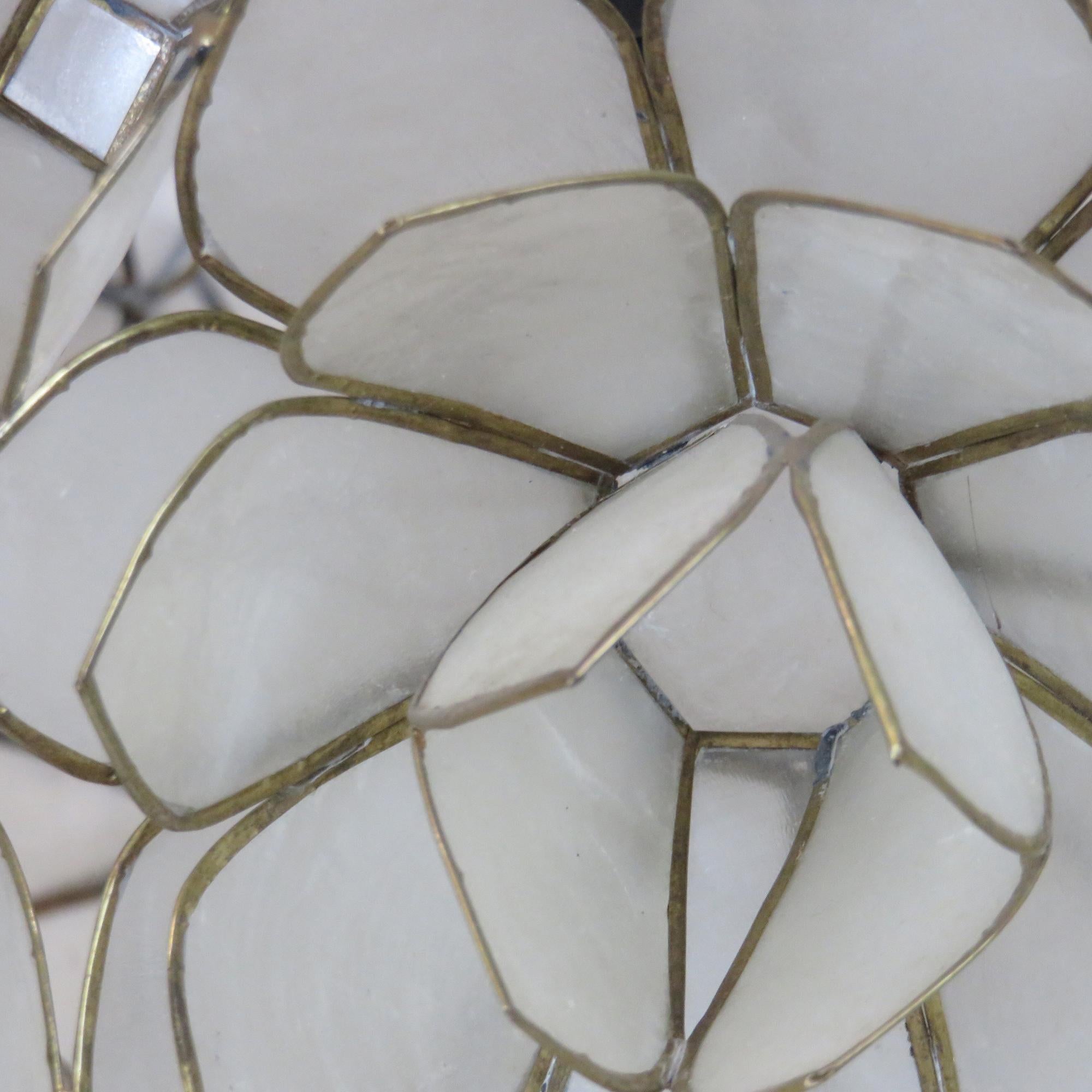 A spherical pendant with a shade made from layered capiz shell petals arranged in a lotus-like form. The translucent shells soften the light and create a warm, ambient glow. Suspended from a chain, the fixture reflects the floral-inspired designs