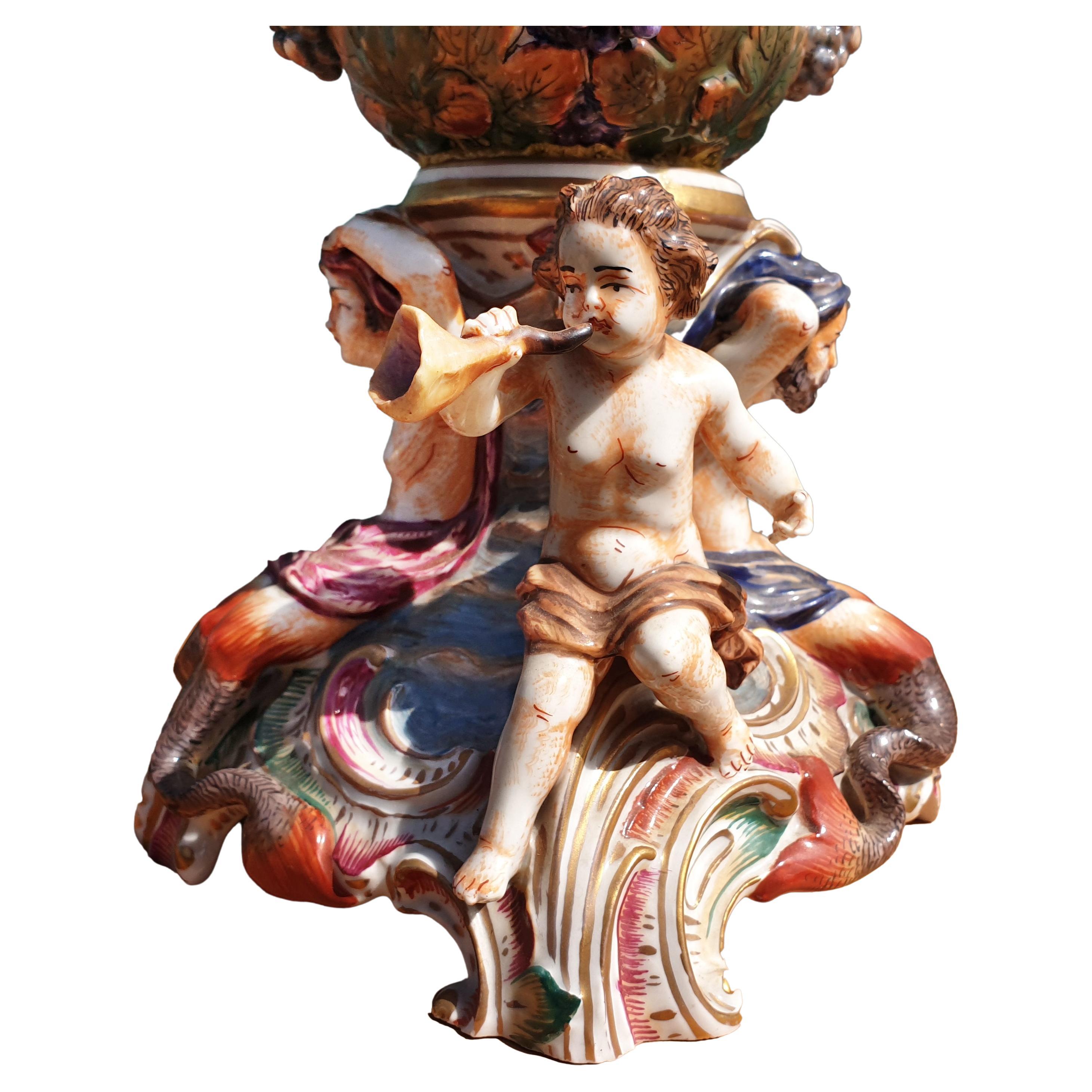 An impressive Capodimonte vase depicting figures, flowers and leaves in finest relief work. The hand crafted vase is hand painted in vivid colors and is partly gilded. The vase is adorned with two figural handles in the form of scantily clad young