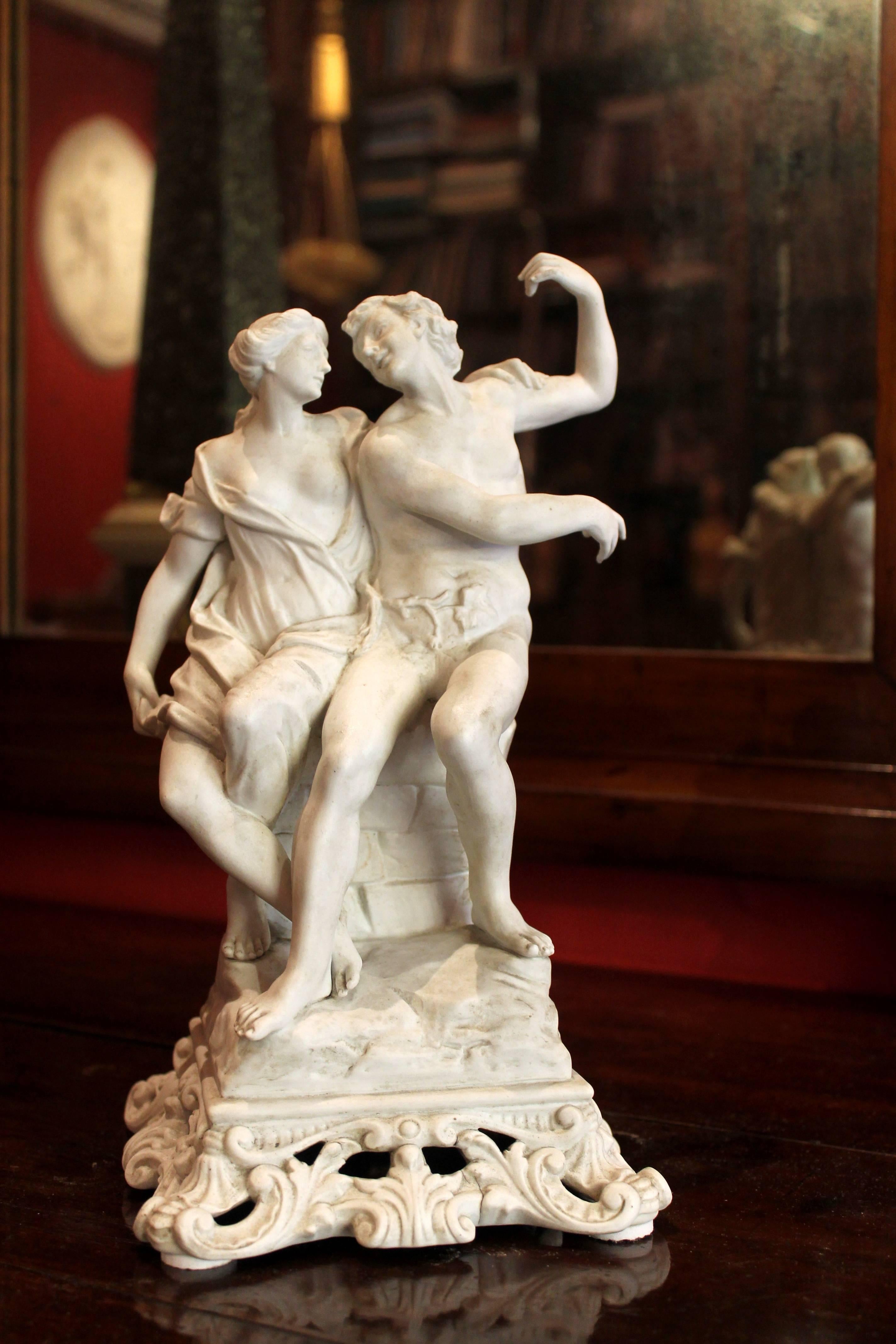 A lovely antique Italian Capodimonte white porcelain biscuit male and female figurines sculptured in the round depicting in a very romantic moment. This centrepiece group features two nude draped young lovers sitting on a pedestal sculptured as a