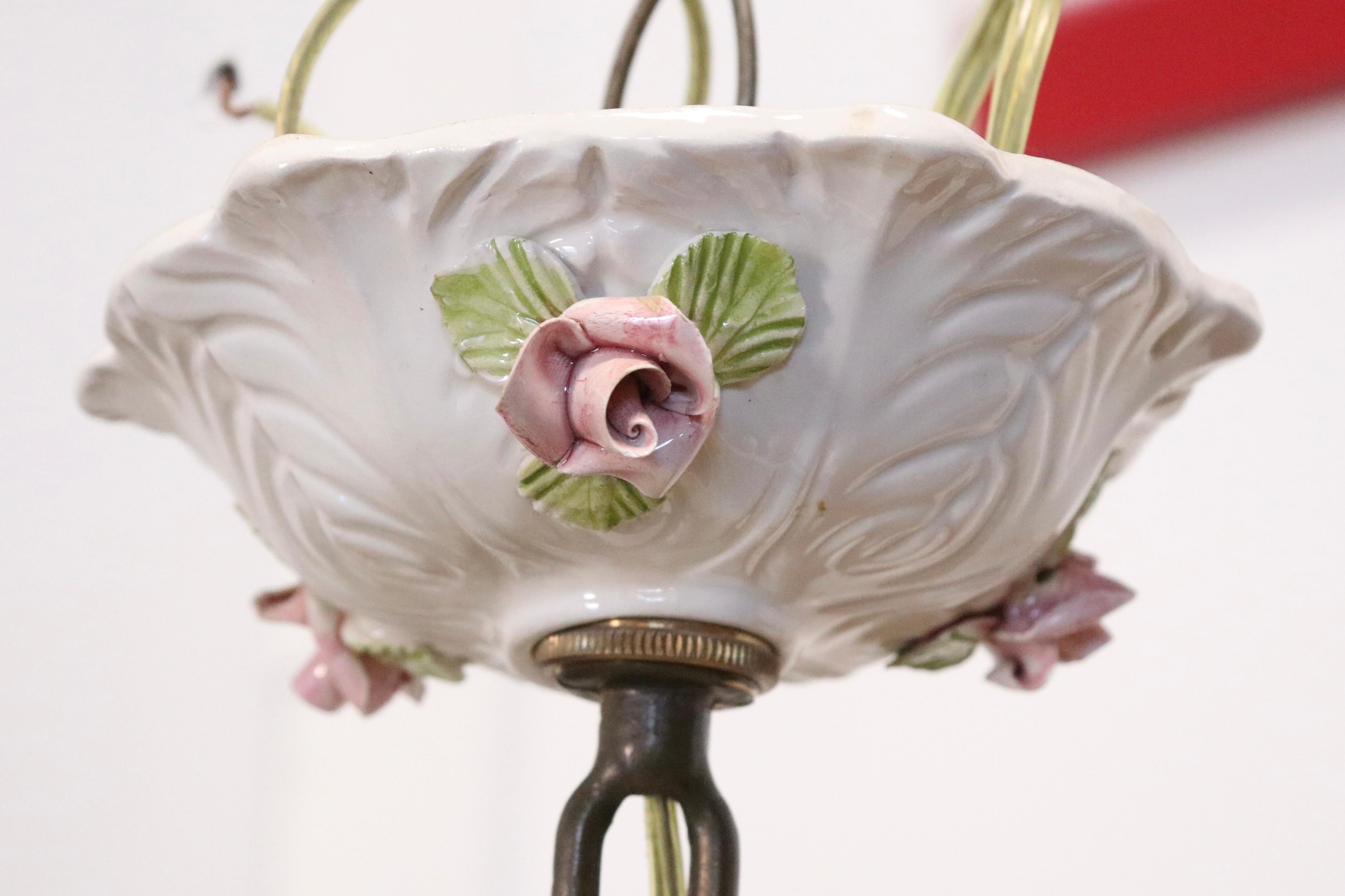 A fanciful white porcelain six arm chandelier in the style of Capodimonte.

Features a ribbed frame decoated with rose florettes and cherubs, complemented by a gold finial. 

Made in Italy, circa 1960.