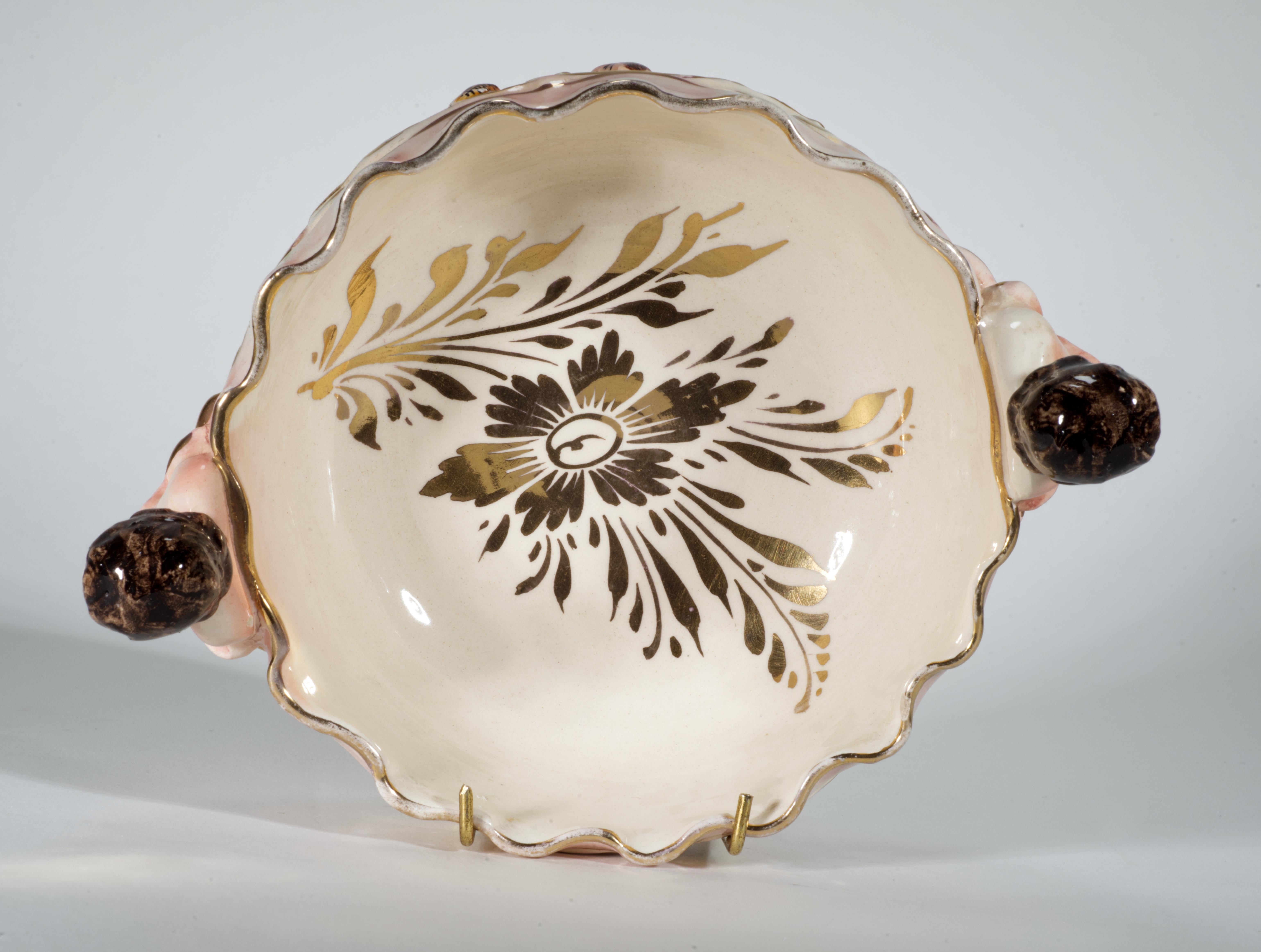  Rare vintage majolica footed bowl is decorated with raised reliefs of cherubs playing in garden on both front and back sides of the bowl; two handles in shape of cherubs peeking from large abstract leaves complement the ornate design. The inside of