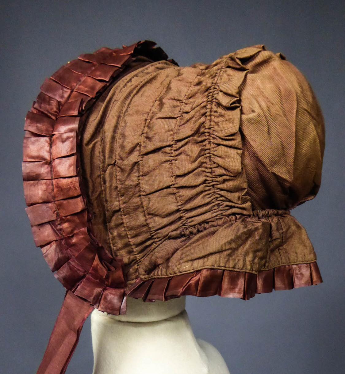 Circa 1860
France

Capote with bavolet in taffeta for a girl of 10/12 years dating from the Victorian period. Spinach green taffeta on framework in iron hoops and ecru tarlatan lining. Work of bouillonné pleats. Closing with large knotted taffeta