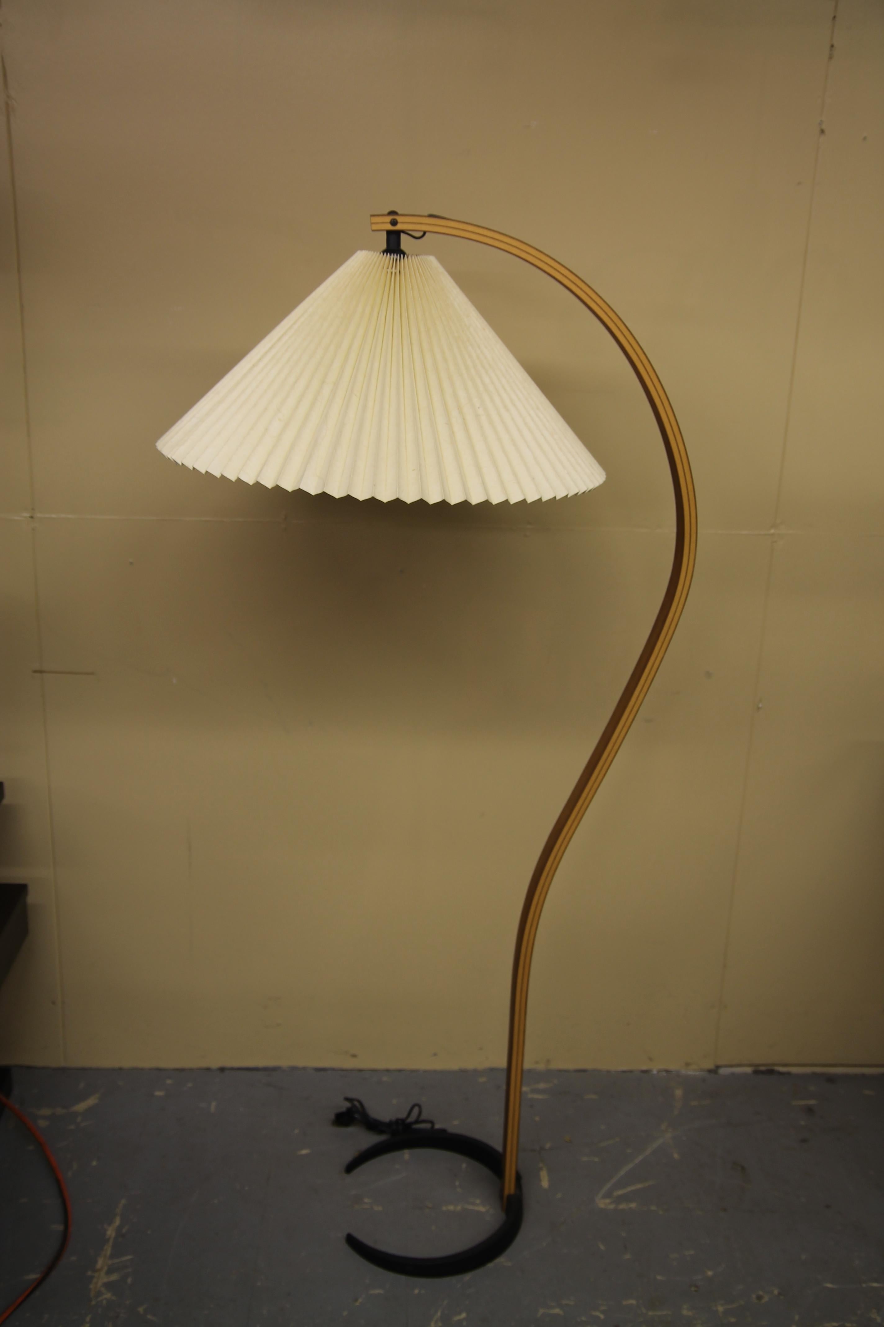 Bentwood floor lamp by Caprani Light A/S with original pleated shade. In its snaking ascent with birch frame encompasses the angular shade. Lamp sets on a crescent shaded cast iron base.