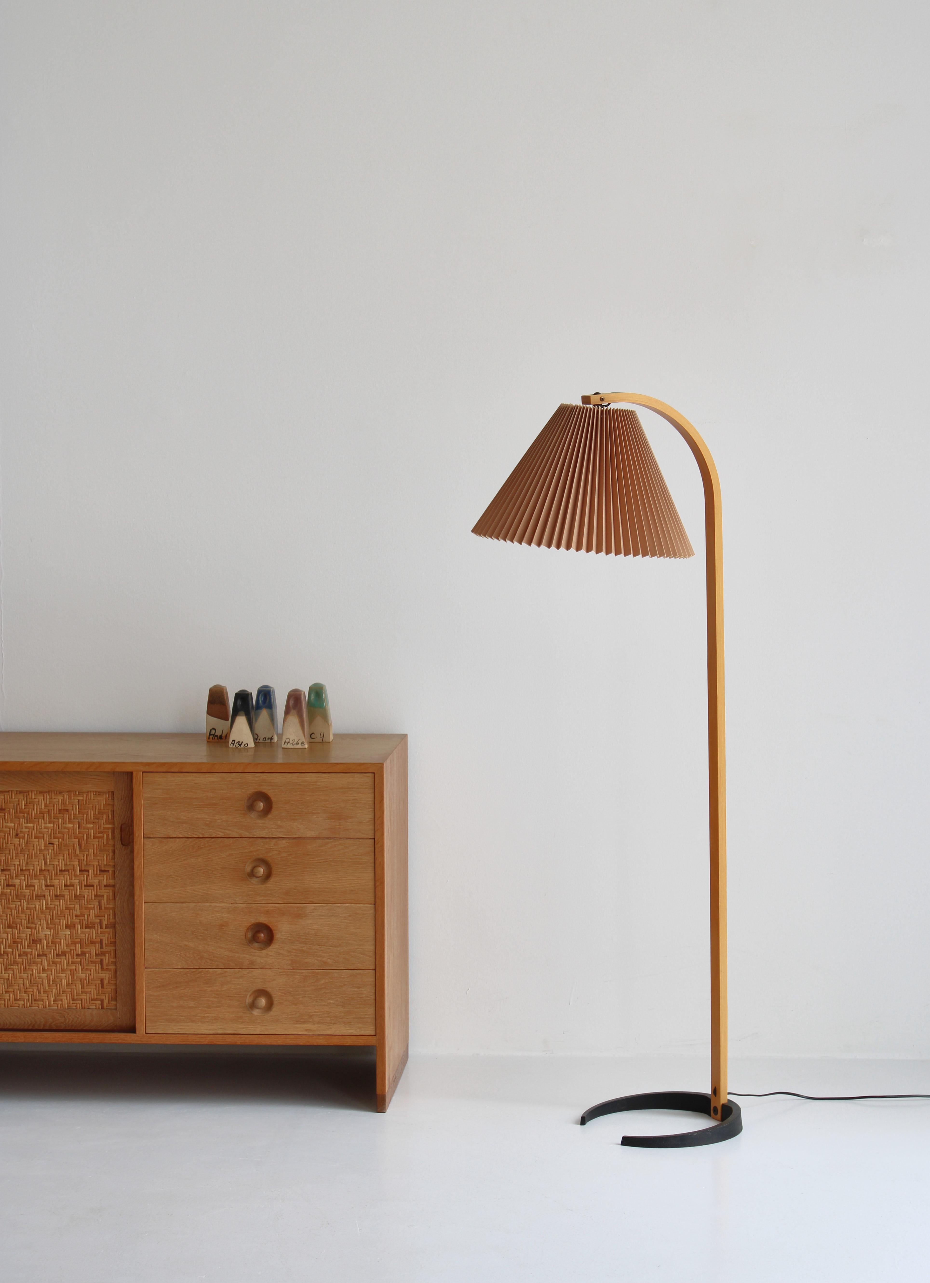 An original Caprani Lights floor lamp designed by Danish architect Mads Caprani in the 1970s. This vintage lamp features a sculptural bent plywood stand with an elegant curve, a cast iron crescent shaped base, and original hand pleated blush linen
