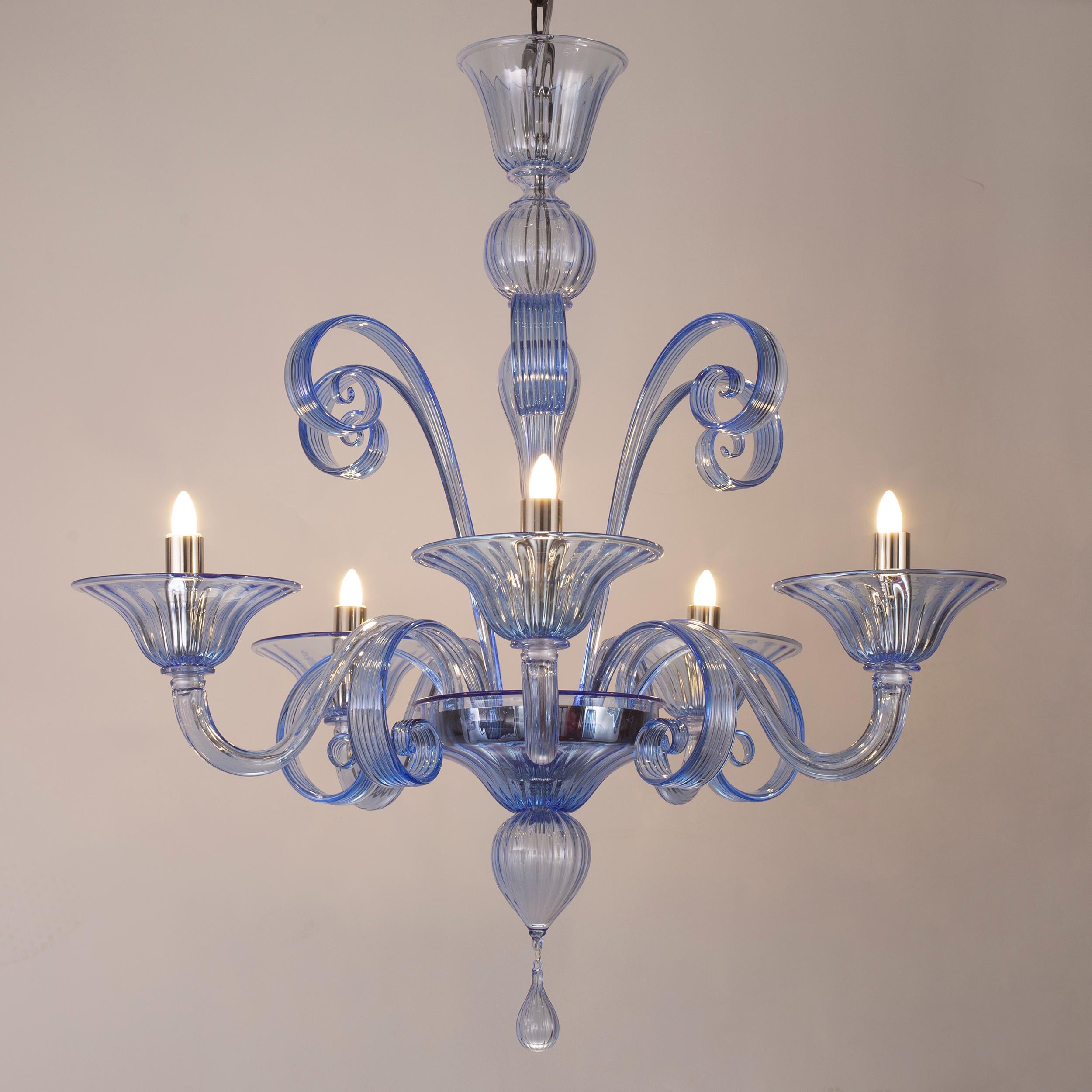 Capriccio by Multiforme is a 5 lights chandelier, in blue artistic glass, with curly ornamental elements.
Inspired by the Classic Venetian tradition it is characterized by a central column where many blown glass “pastoral” elements are installed.