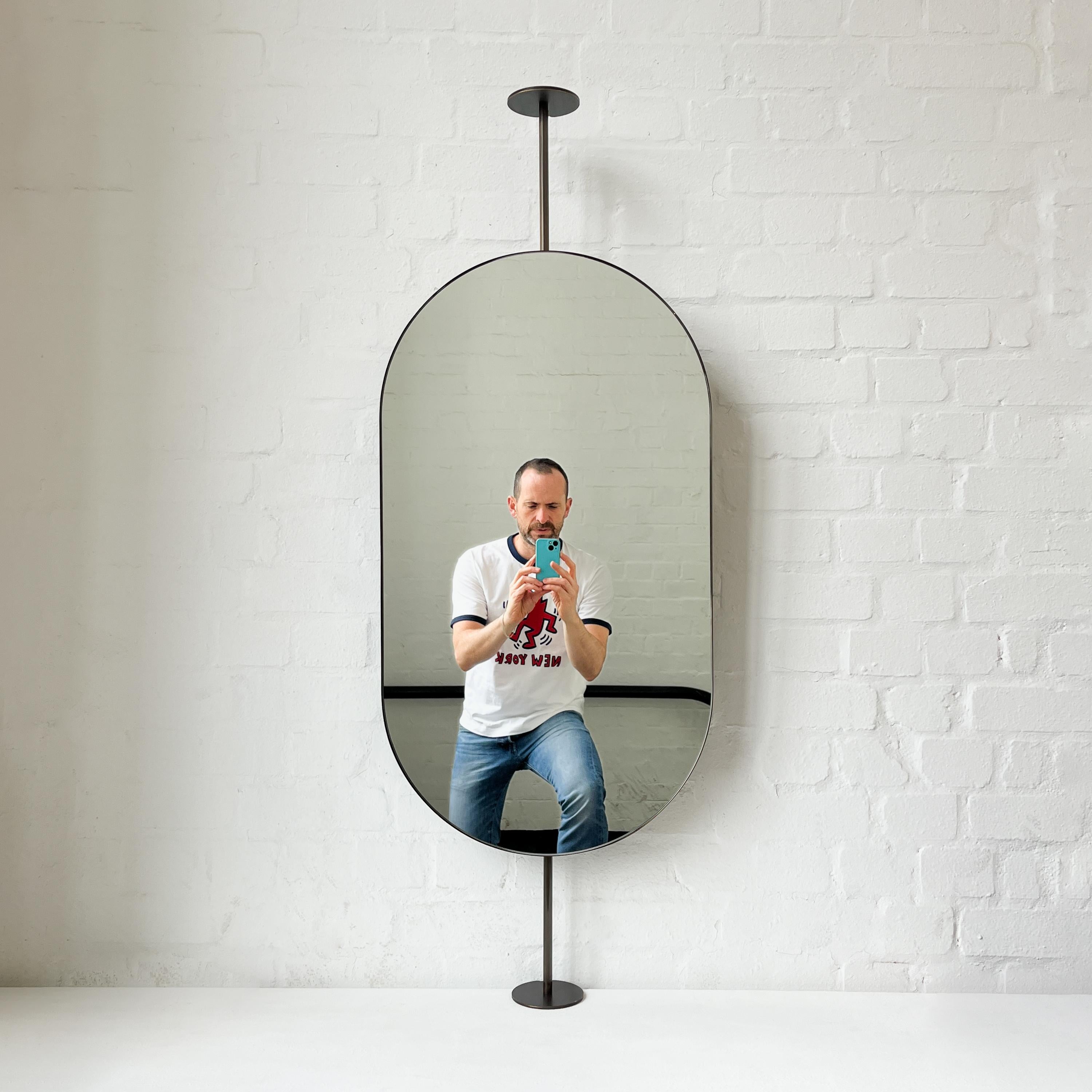 Contemporary countertop to ceiling attached Capsula™ pill shaped mirror with a handcrafted bronze patina brass frame. Designed and handcrafted in London, UK. This mirror is fully customisable.

Dimensions:

H 83.2cm x W 45.7cm x D 3cm (Drop 15.6cm,