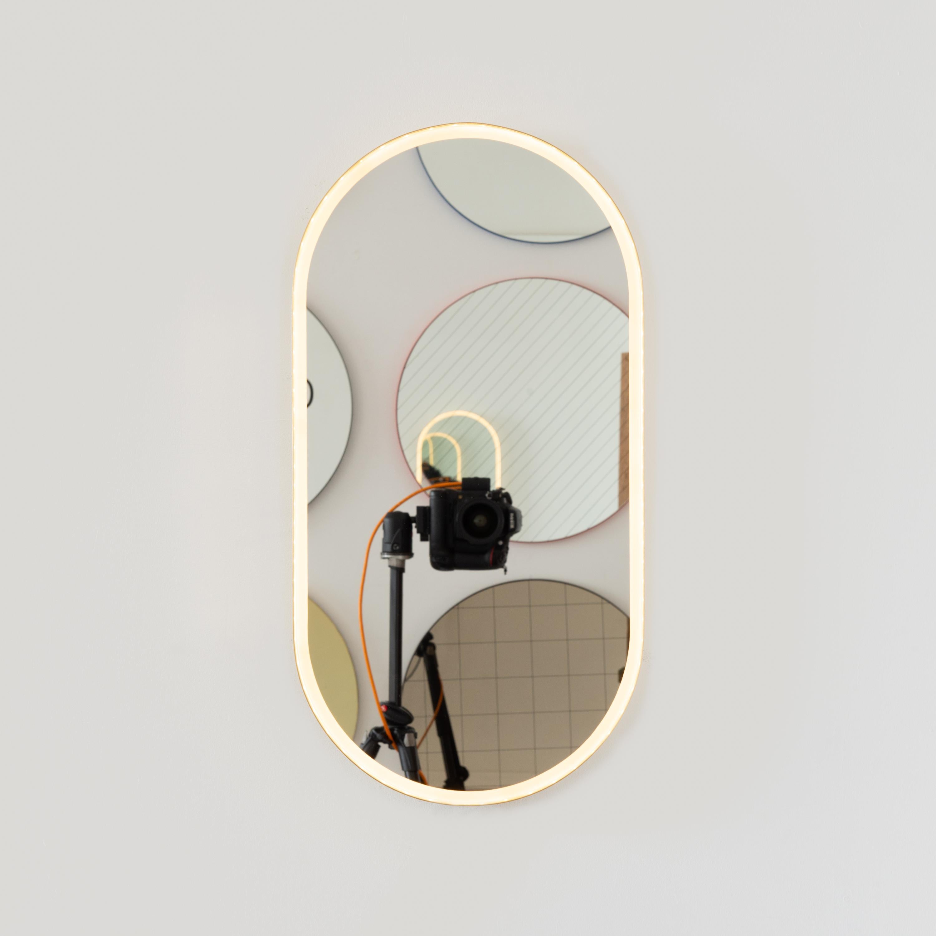 Moderner, handgefertigter, von vorne beleuchteter, kapselförmiger Spiegel mit einem eleganten Rahmen aus gebürstetem Messing. Entworfen und handgefertigt in London, UK.

Die mittelgroßen, großen und extragroßen Spiegel (37 cm x 56 cm, 46 cm x 71 cm