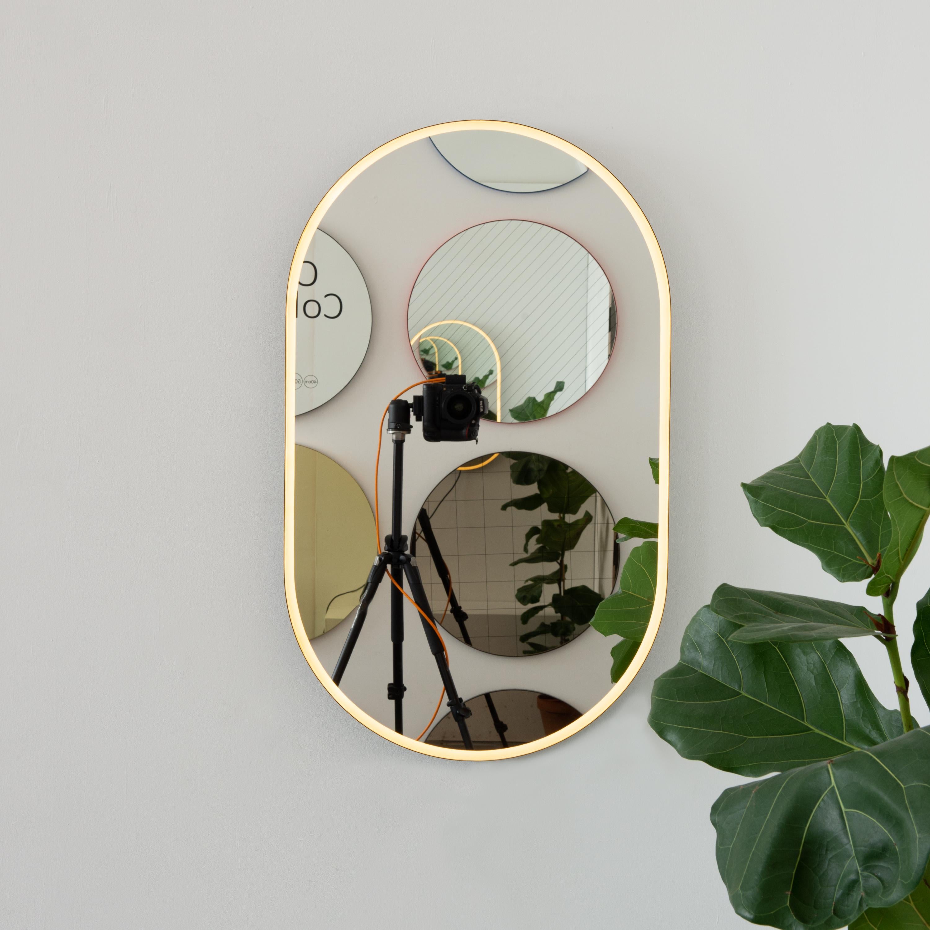 Moderner, handgefertigter, von vorne beleuchteter, kapselförmiger Spiegel mit einem eleganten, bronzefarben patinierten Messingrahmen. Entworfen und handgefertigt in London, UK.

Je nach Größe des Spiegels mit einem Messinghaken oder einer