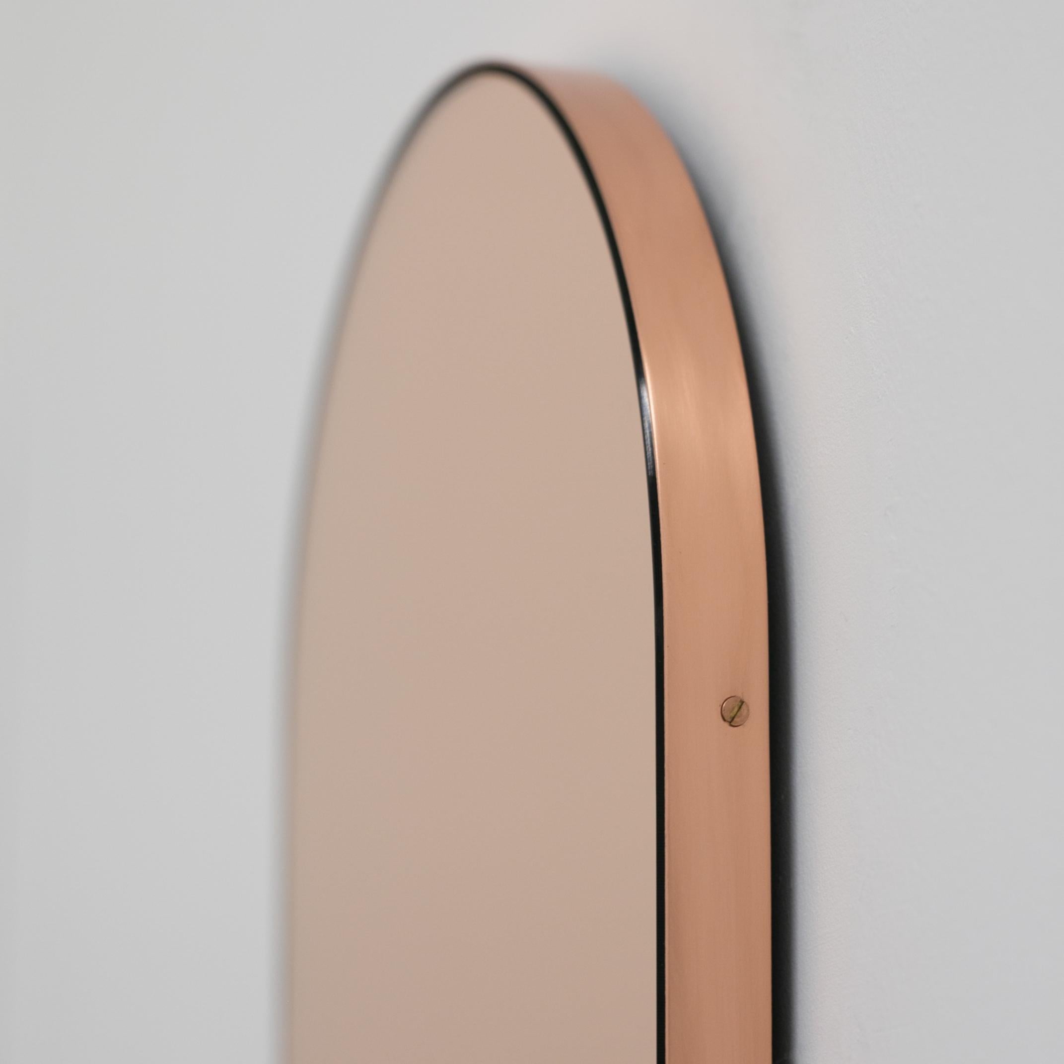Contemporary capsule shaped rose gold or peach mirror with an elegant copper frame. Designed and handcrafted in London, UK. The detailing and finish, including visible copper-plated screws, emphasise the craft and quality feel of the mirror, a true