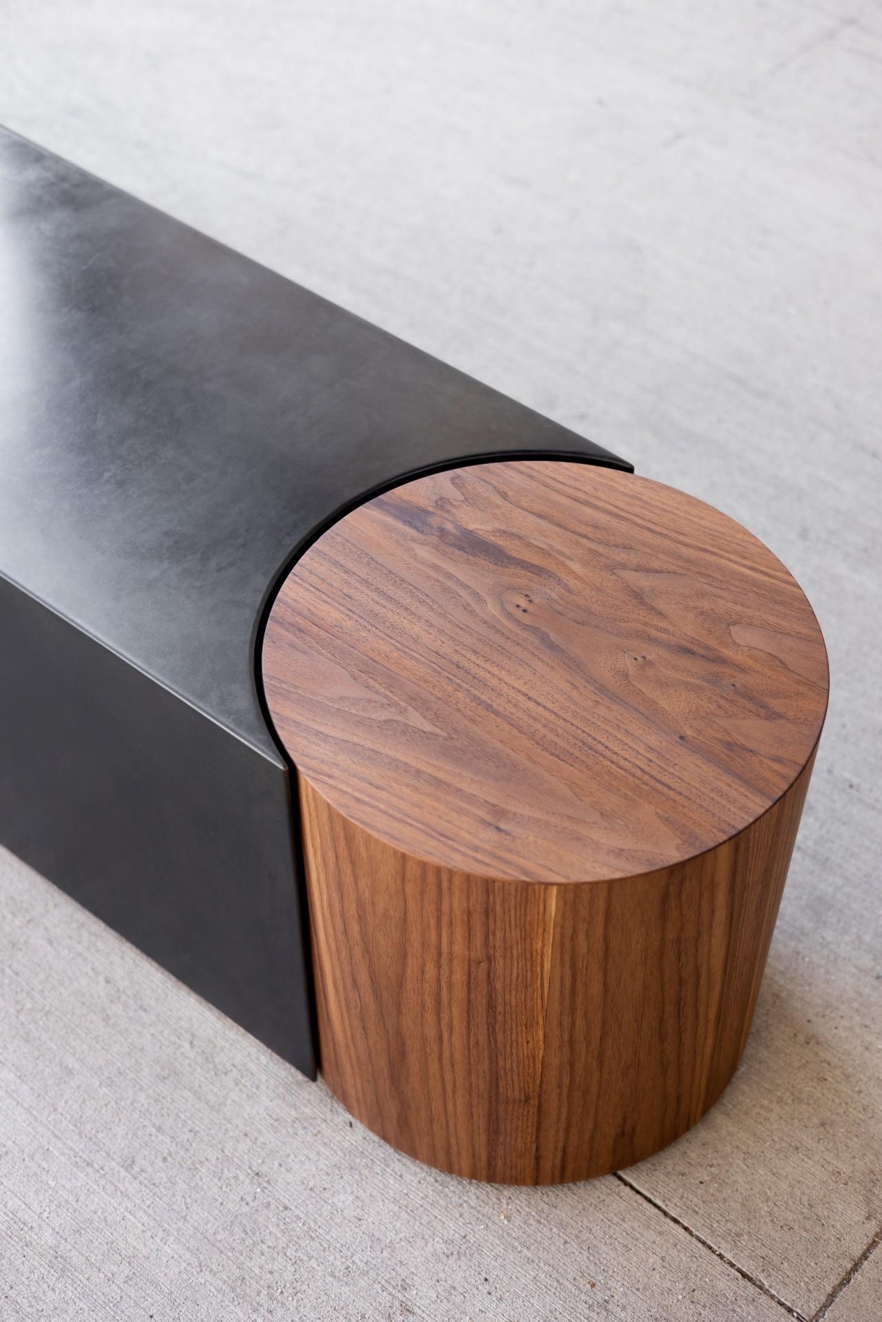 The Capsule Bench brings together a deep rich patinated steel body with a warm walnut side table. 

The table is independent of the steel so it can be pulled out and used along with the bench and then put back in its place to create the complete