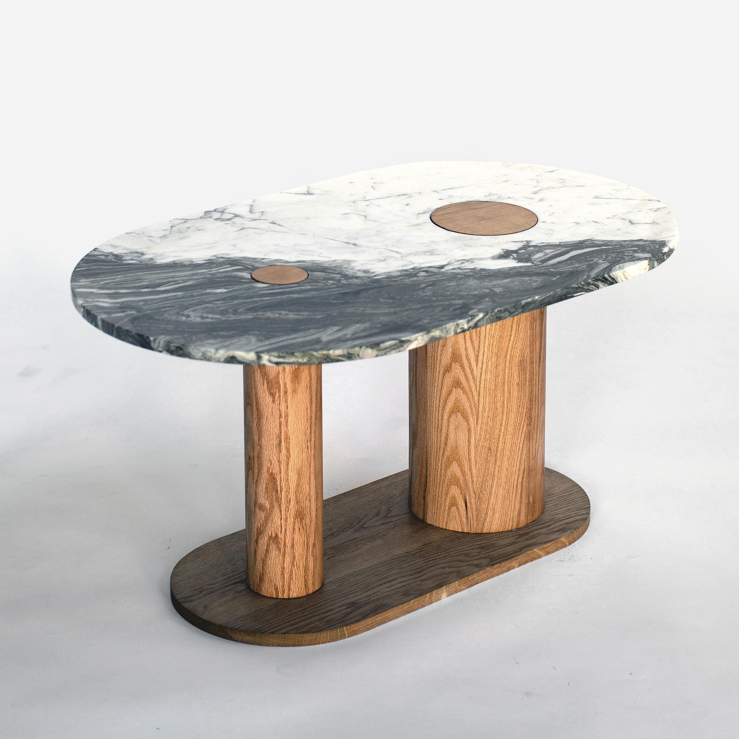 This coffee table comes in a shocking two-toned marble, cream white and green-tinted charcoal. Two cutouts in the marble top reveal the materiality of the asymmetrical legs below. The legs, made in solid white oak, are hand-lathed with an oiled