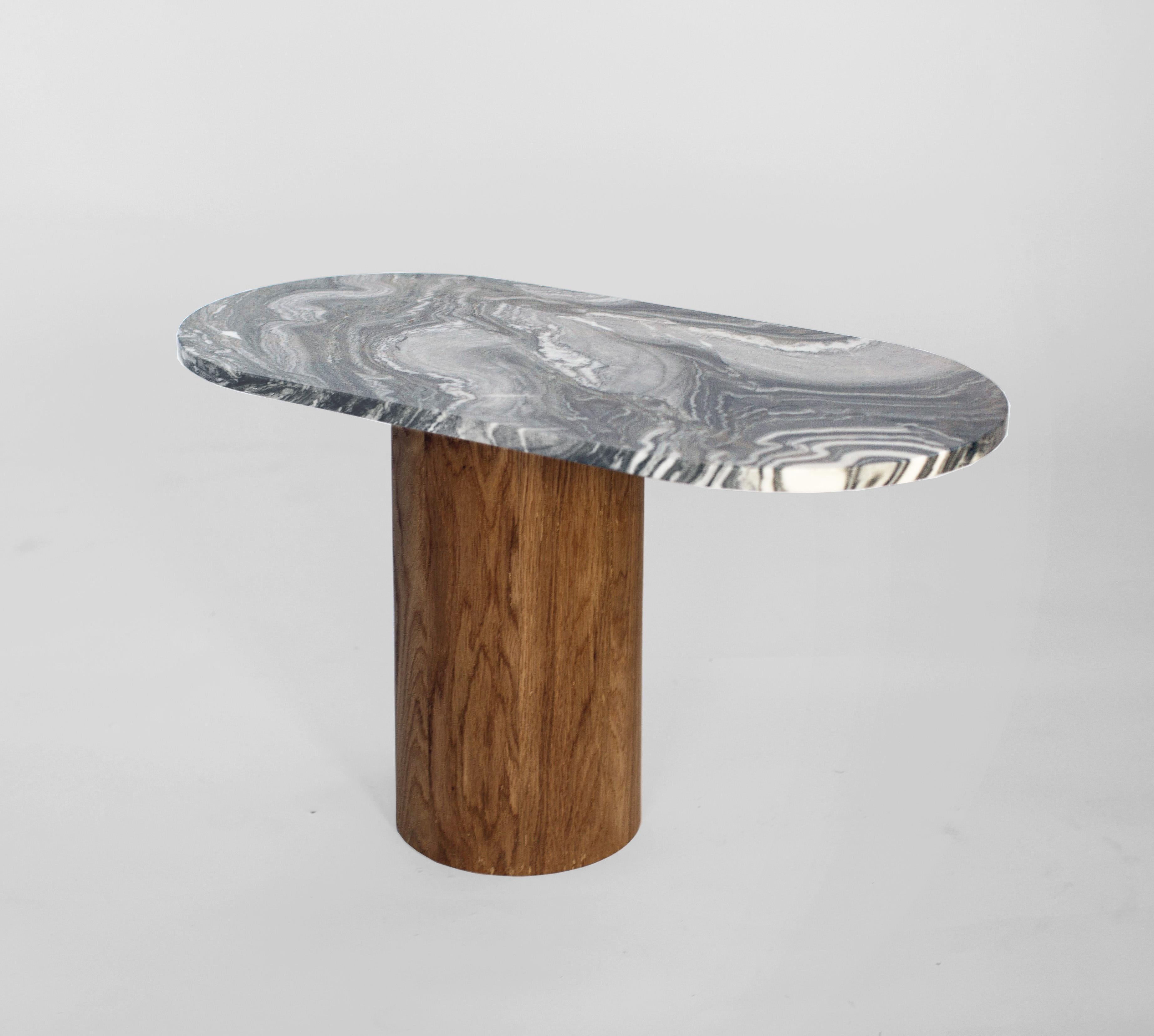 Cette table basse ou d'appoint est réalisée dans un marbre riche et foncé avec des veines laiteuses. Le plateau en marbre est doté d'une base décalée par rapport à son centre qui est fabriquée en chêne blanc massif latté à la main avec une finition
