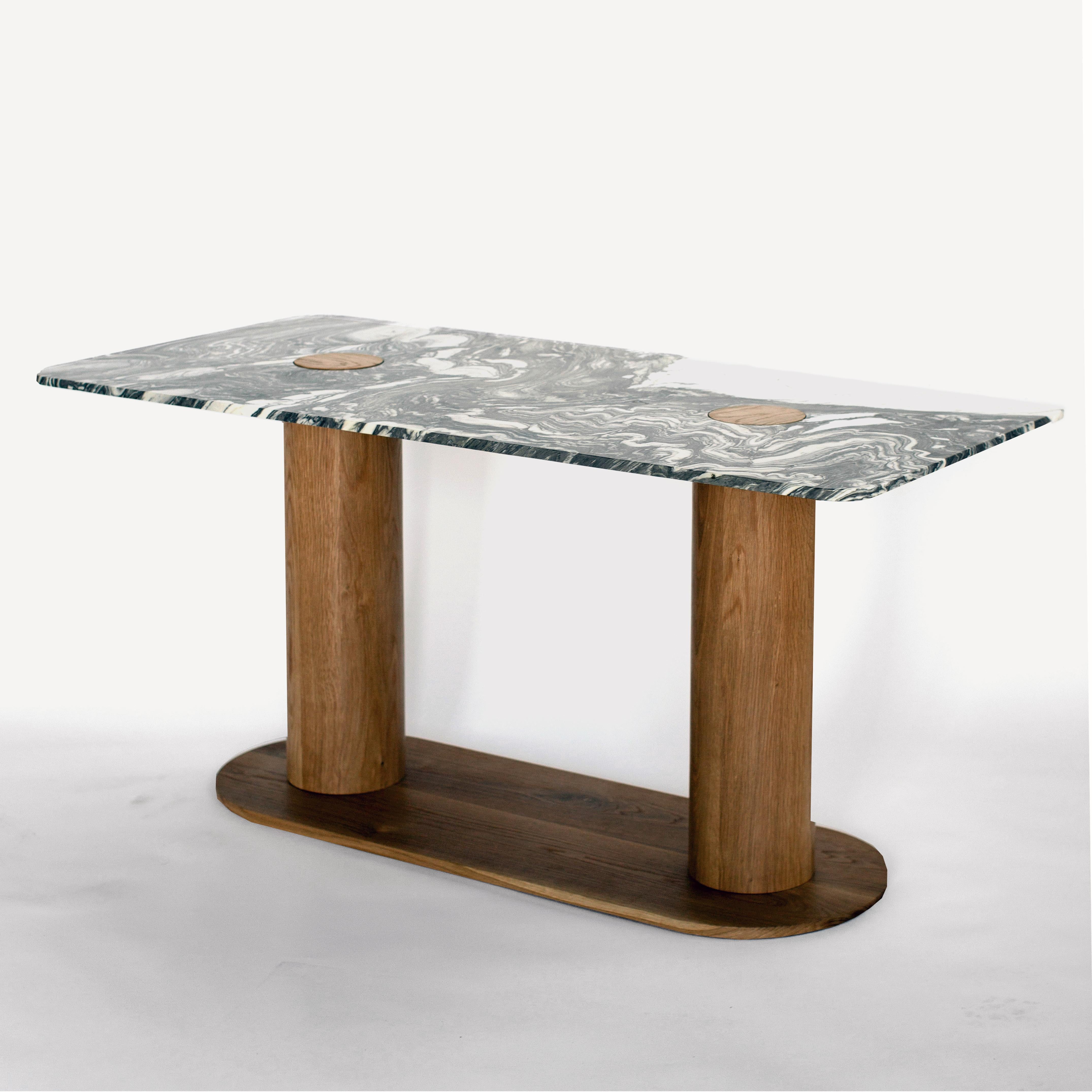 This compact dining table comes in a marble with expressive green/gray and cream white swirls. Two cutouts in the marble top reveal the materiality of the solid white oak legs below. These are hand-lathed with an oiled finish and sit on a matching