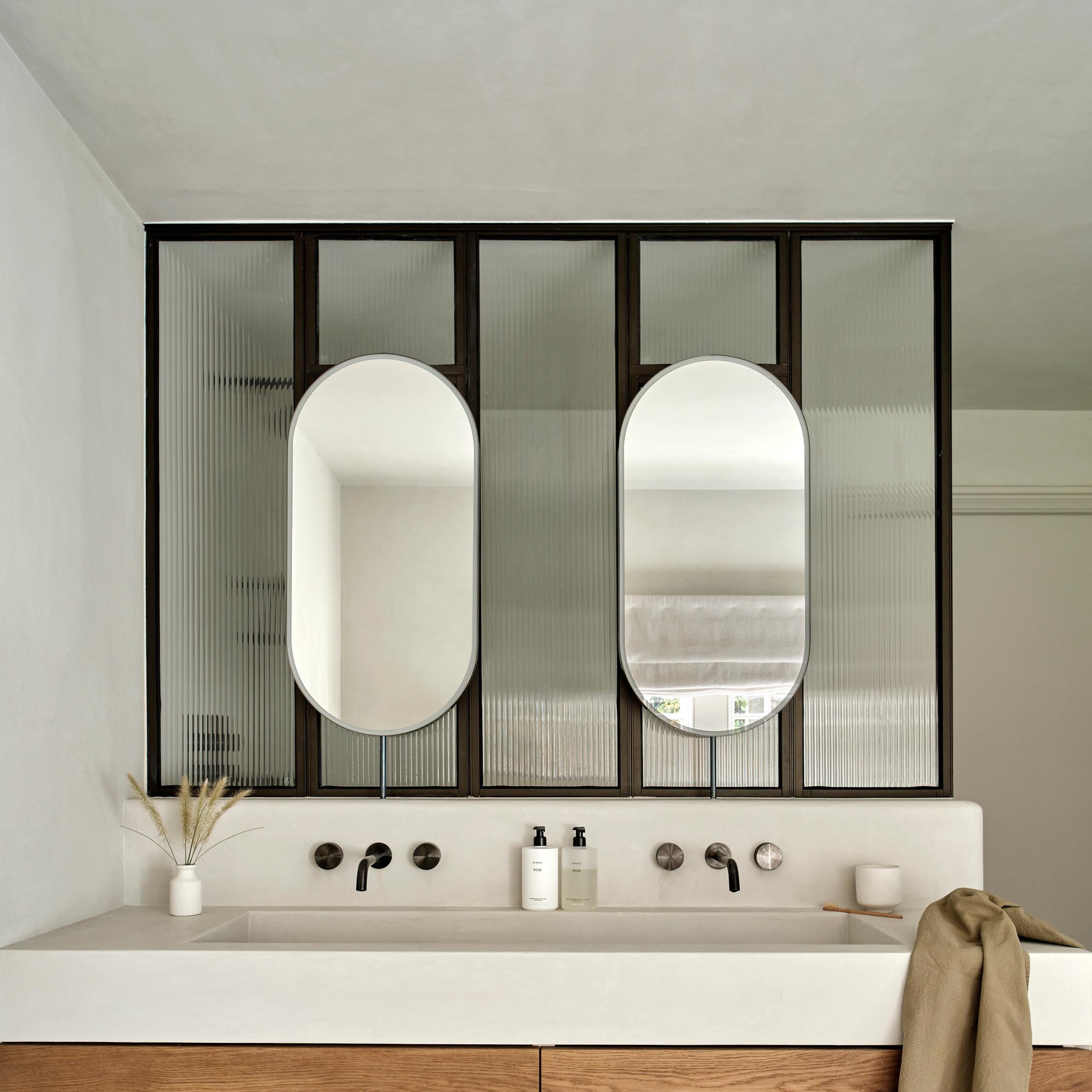 Miroir de comptoir Capsula™ contemporain éclairé par l'avant en forme de pilule avec un cadre, un bras et une contre-plaque minimalistes en acier inoxydable noirci. Conçu et fabriqué à Londres, au Royaume-Uni. Ce miroir est entièrement