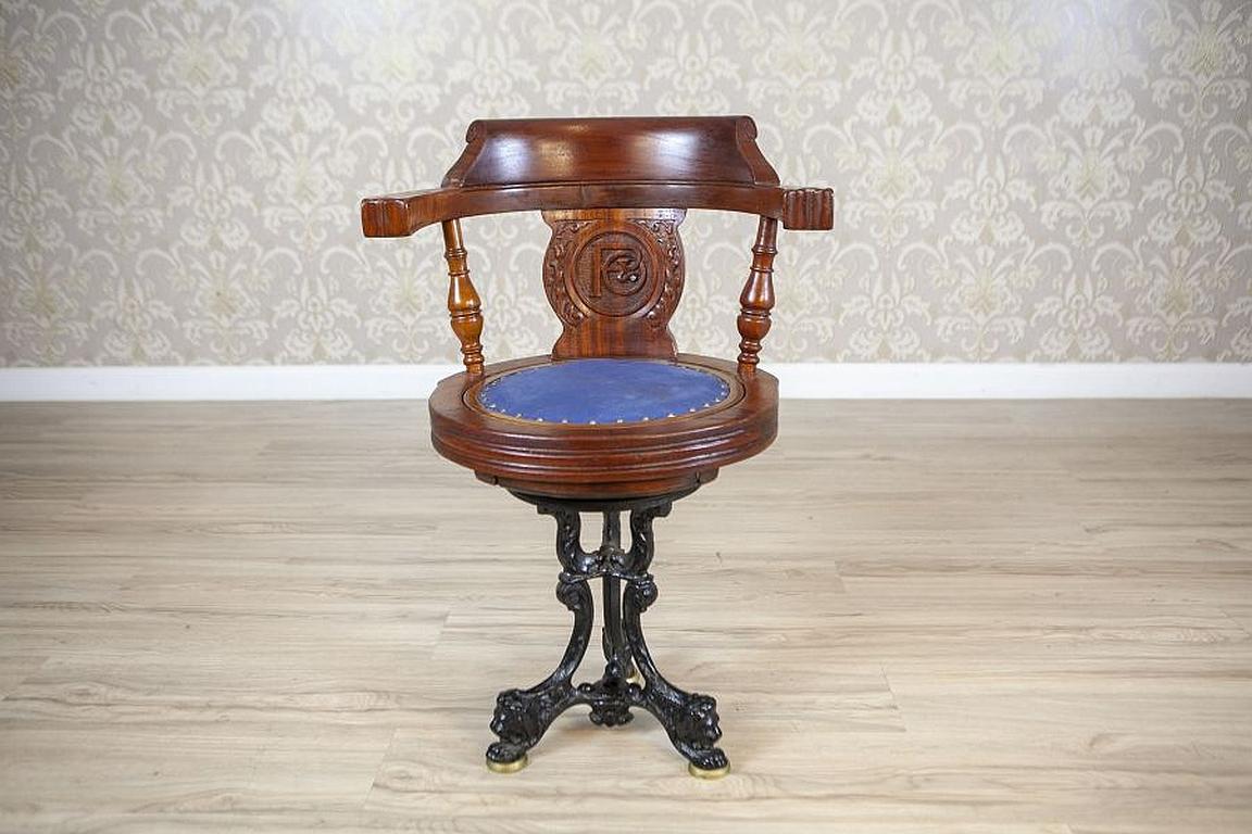 Captain Armchair - Early-20th Century Wooden Desk Chair With Soft Seat

A wooden chair with a soft seat and a carved, arched backrest that transitions into armrests, ending with a heavy cast-iron base with legs shaped like lion heads. It is called