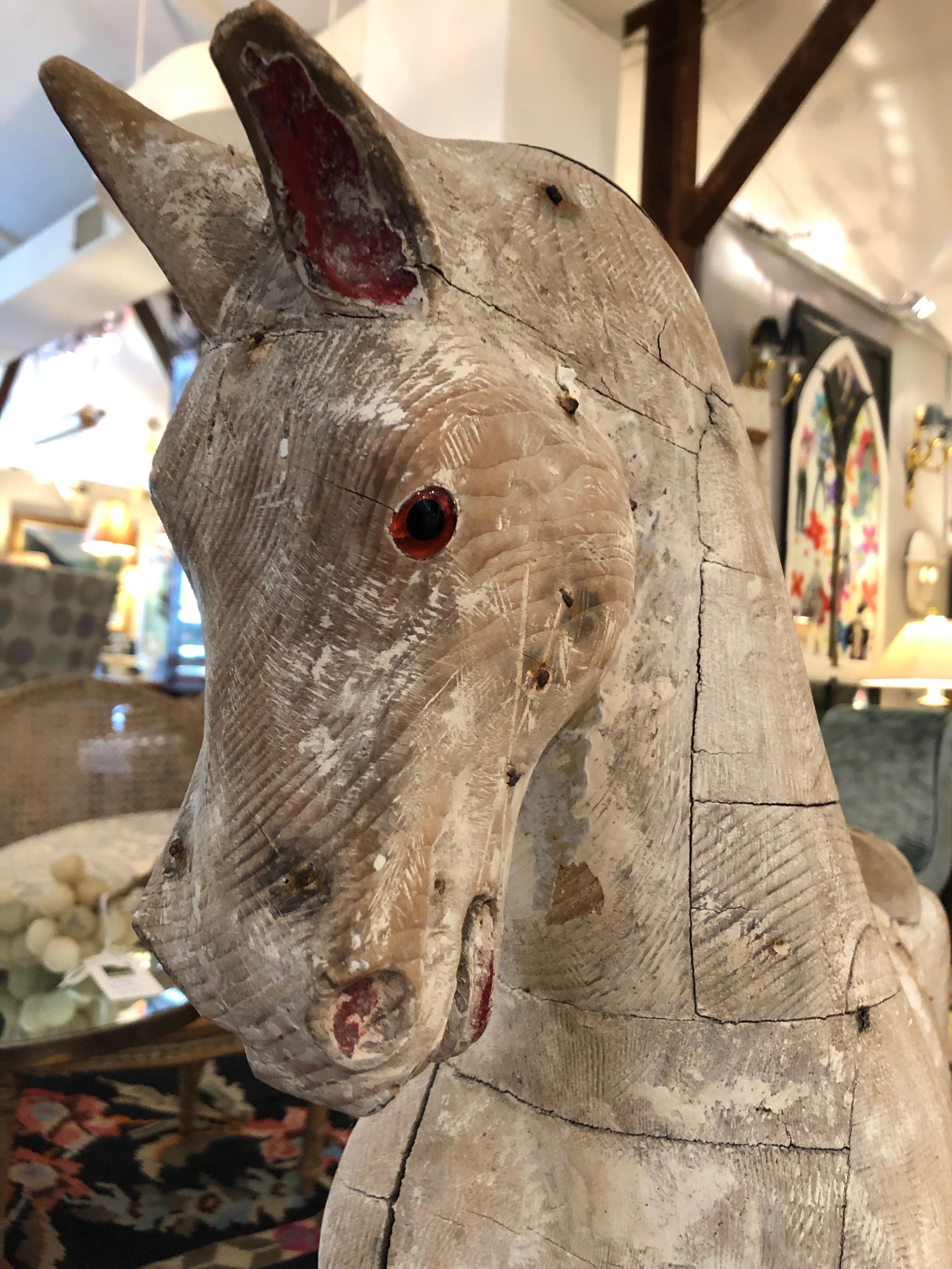A wonderful hand carved children's hobby horse with original paint and distressed white washed patina. The eyes are amber glass and the base is natural wood. So beautiful, this is a work of folk art and an impressive decorative accessory.