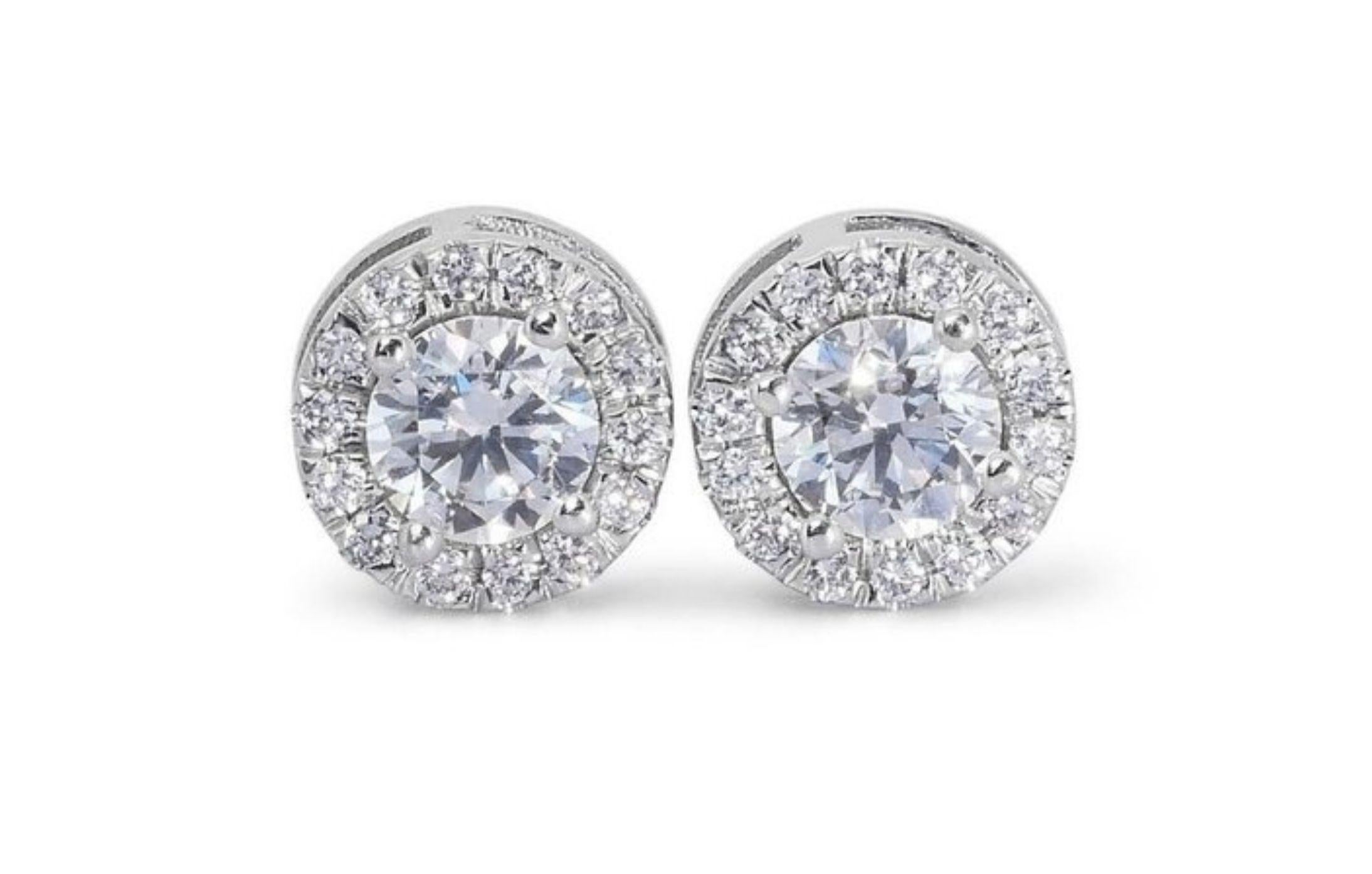 Own a timeless treasure with these exquisite 1 carat diamond earrings, radiating breathtaking brilliance and effortless sophistication with .25 ct side diamonds. Meticulously crafted in 18K white gold, these earrings showcase two dazzling round