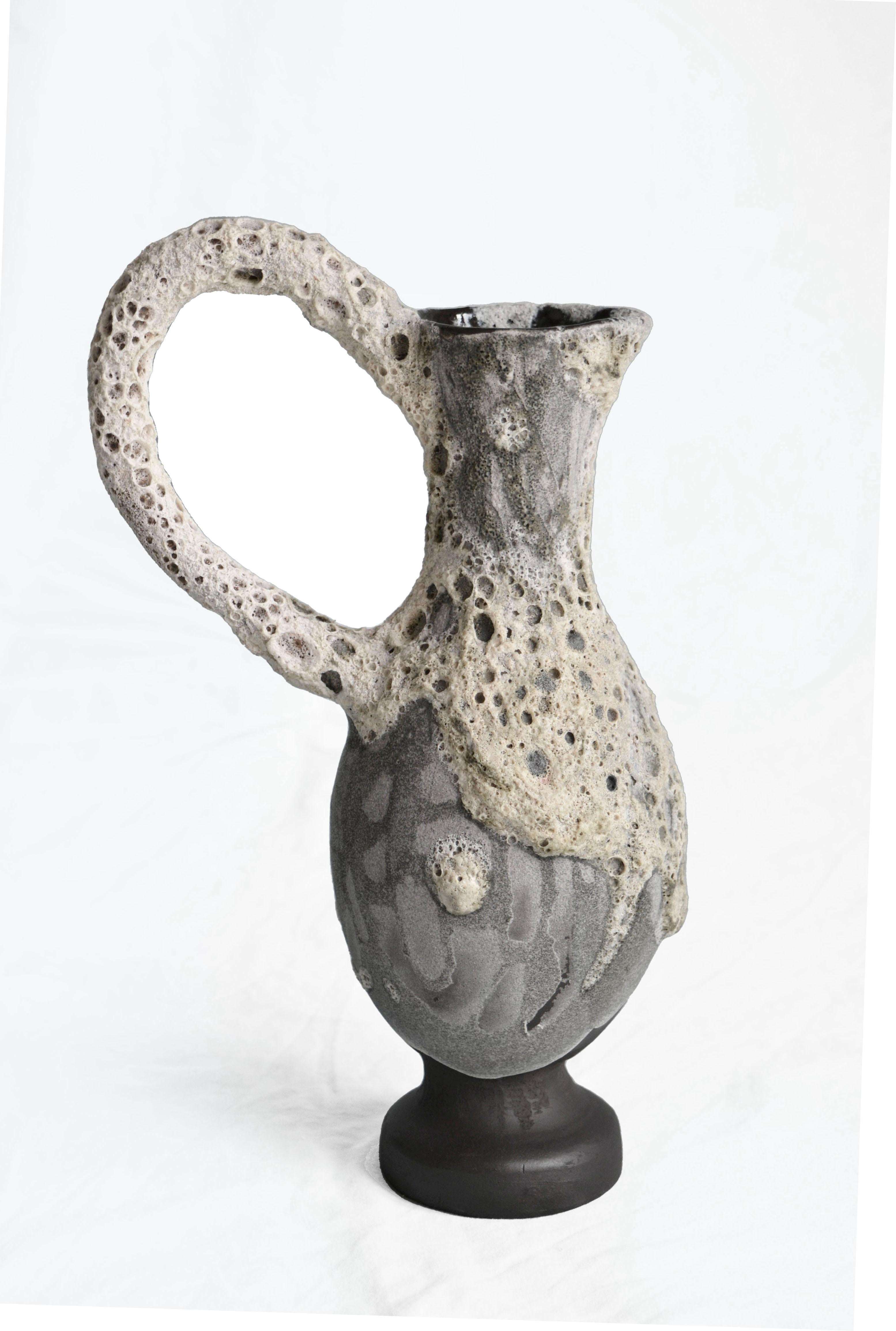 Vaso Carafe 5 di Anna Karountzou
Dimensioni: L. 17 x P. 11,5 x H. 30,5 cm
Materiali: argilla in gres nero, smalto trasparente all'interno, smalto a cratere fatto a mano all'esterno, cottura a 1220

Nata e residente ad Atene, in Grecia, con un