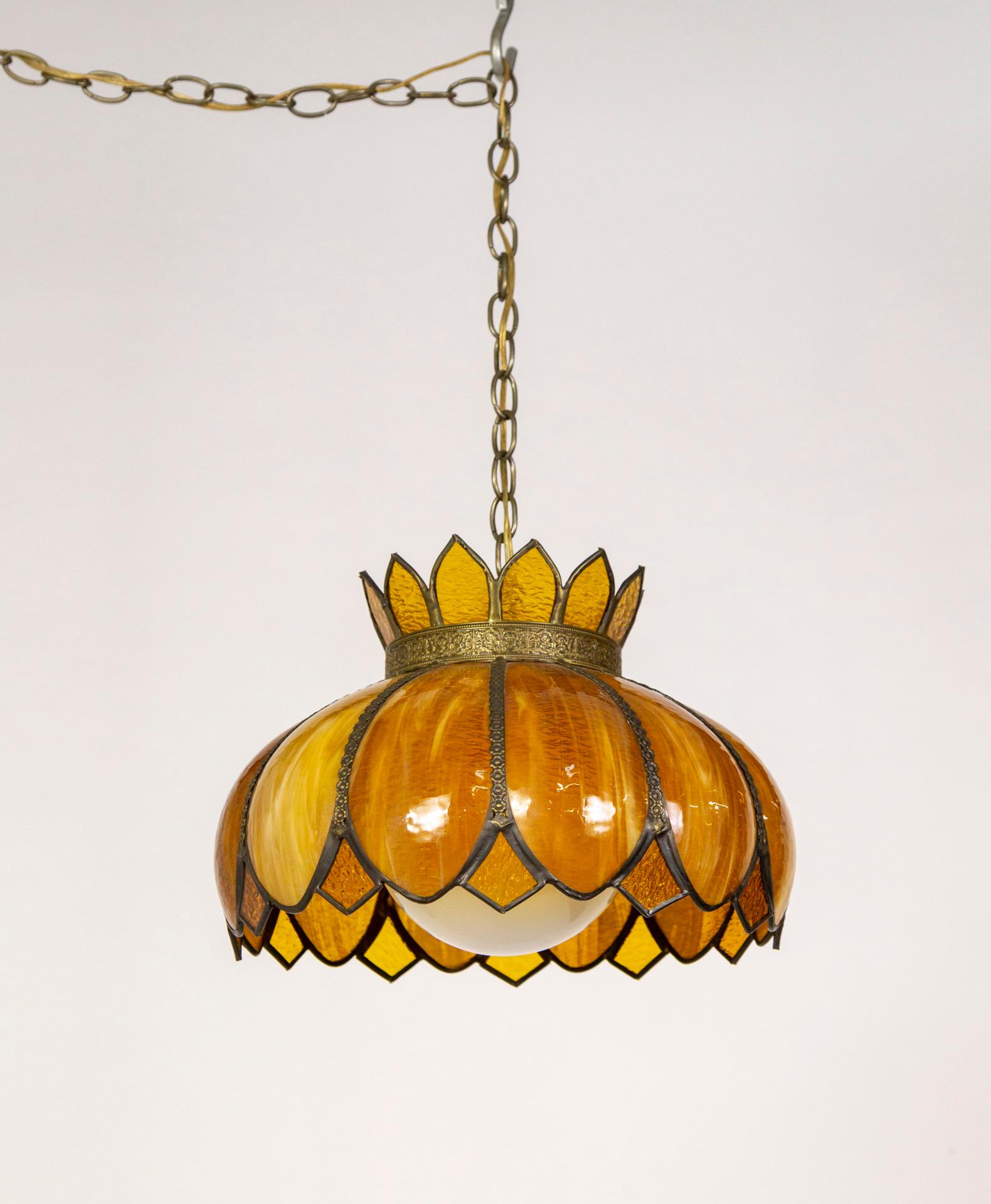 A mid-20th century, hanging light fixture in rich amber, gold, caramel, and yellow streaked slag and stained glass.  It is a lotus shape with scalloped and diamond petals and an ornately pressed brass band at the top and trimming the petals. A milk