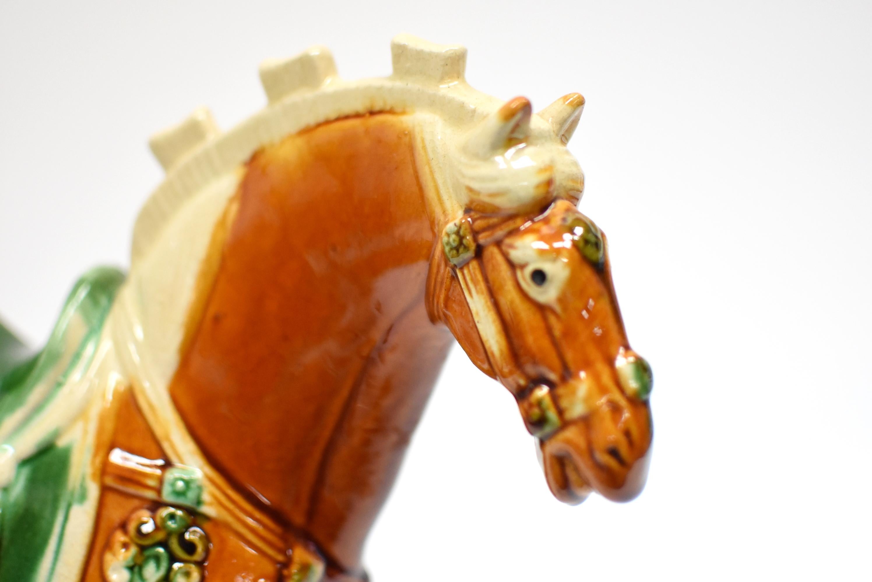 A beautiful caramel color San Cai horse in high gloss. The Sancai technique dates back to the Tang dynasty (618–907AD). His muscles are well defined. His expression vivid. The horse is decorated with fancy bells and a green saddle. Sancai sculptures