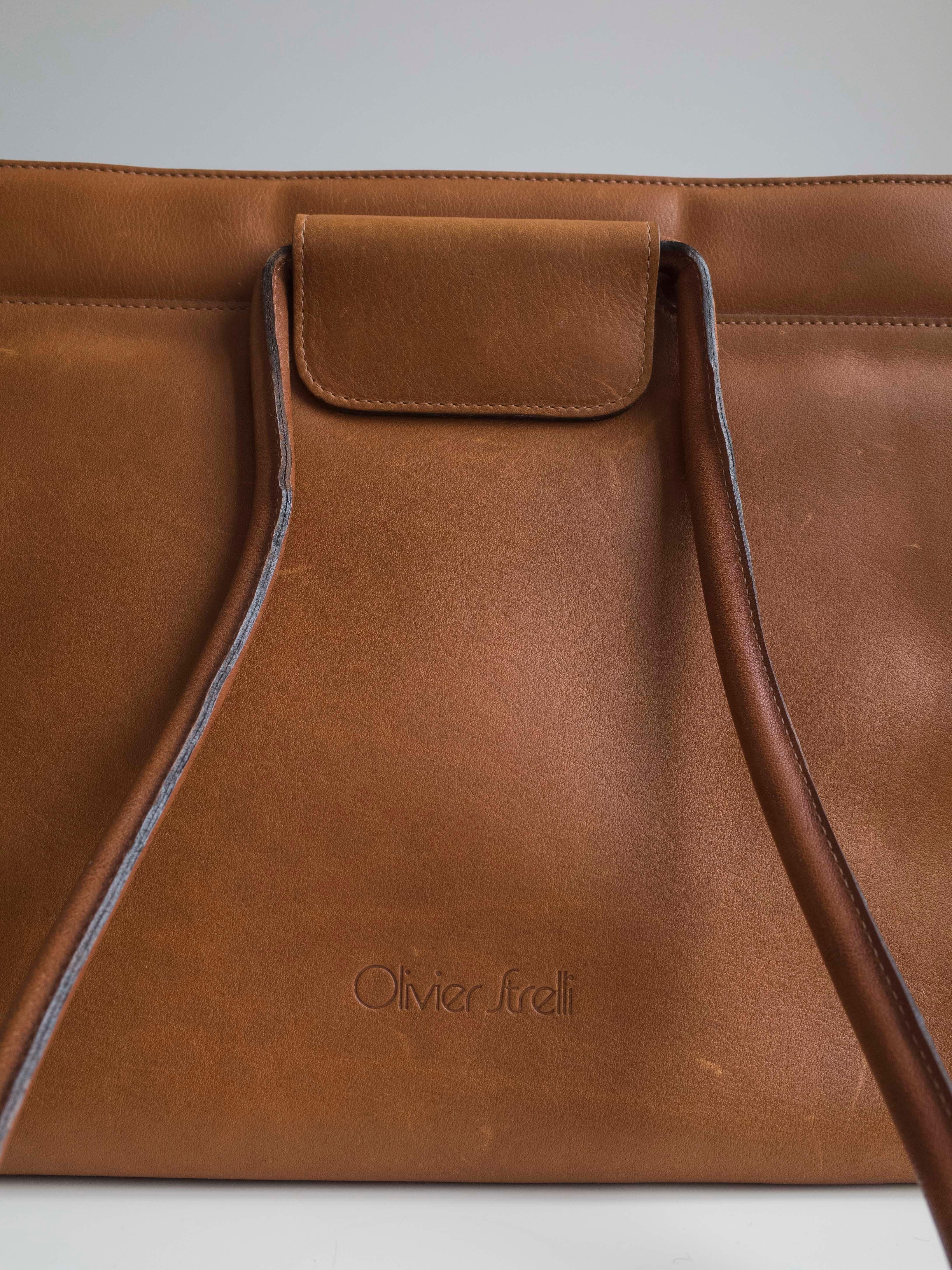 Vintage 1970s handbag by Olivier Strelli. Warm caramel coloured leather with matching top stitch. Embossed logo. Two corded leather straps. 
Double magnetic closure. 
The purse opens to a main leather compartment with a large zippered section. 
Soft