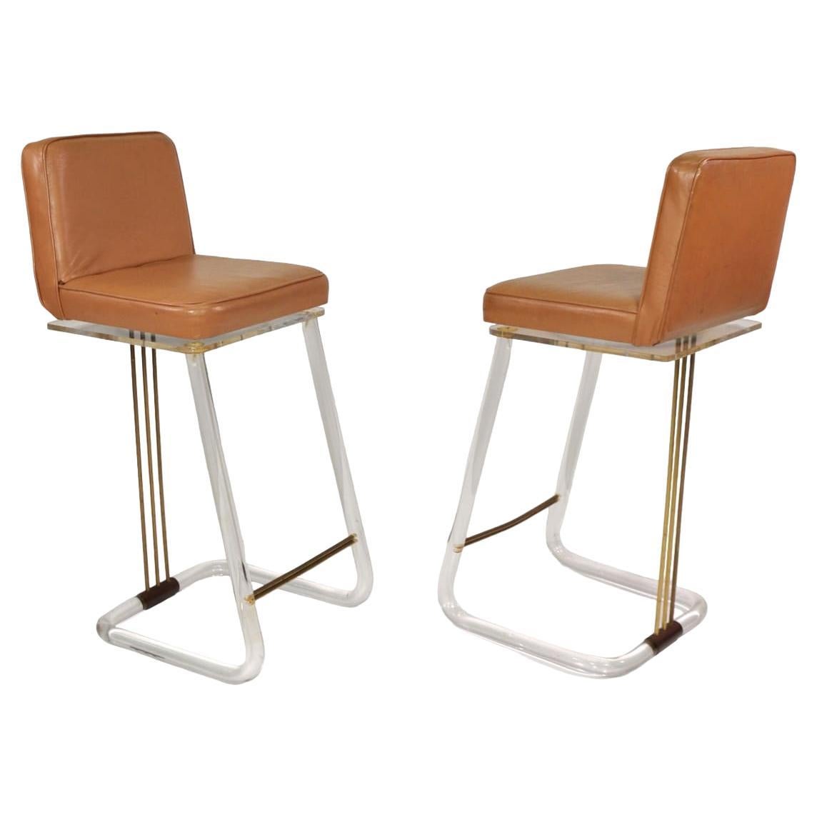 Pair of Mid-Century Modern swiveling bar stools from the 1970s, by Lion in Frost. The vintage stools feature clear tubular lucite frames, brass rod accents and original brown leather seats. Add a touch of Hollywood Regency pizzazz to any interior