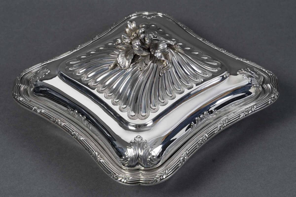 Square vegetable dish with softened corners in the Louis XV style, adorned with a frieze of shells and finely chiseled leaf garlands. The twisted ribbed lid is topped with a handle in the shape of a bouquet of naturalistic flowers and foliage.