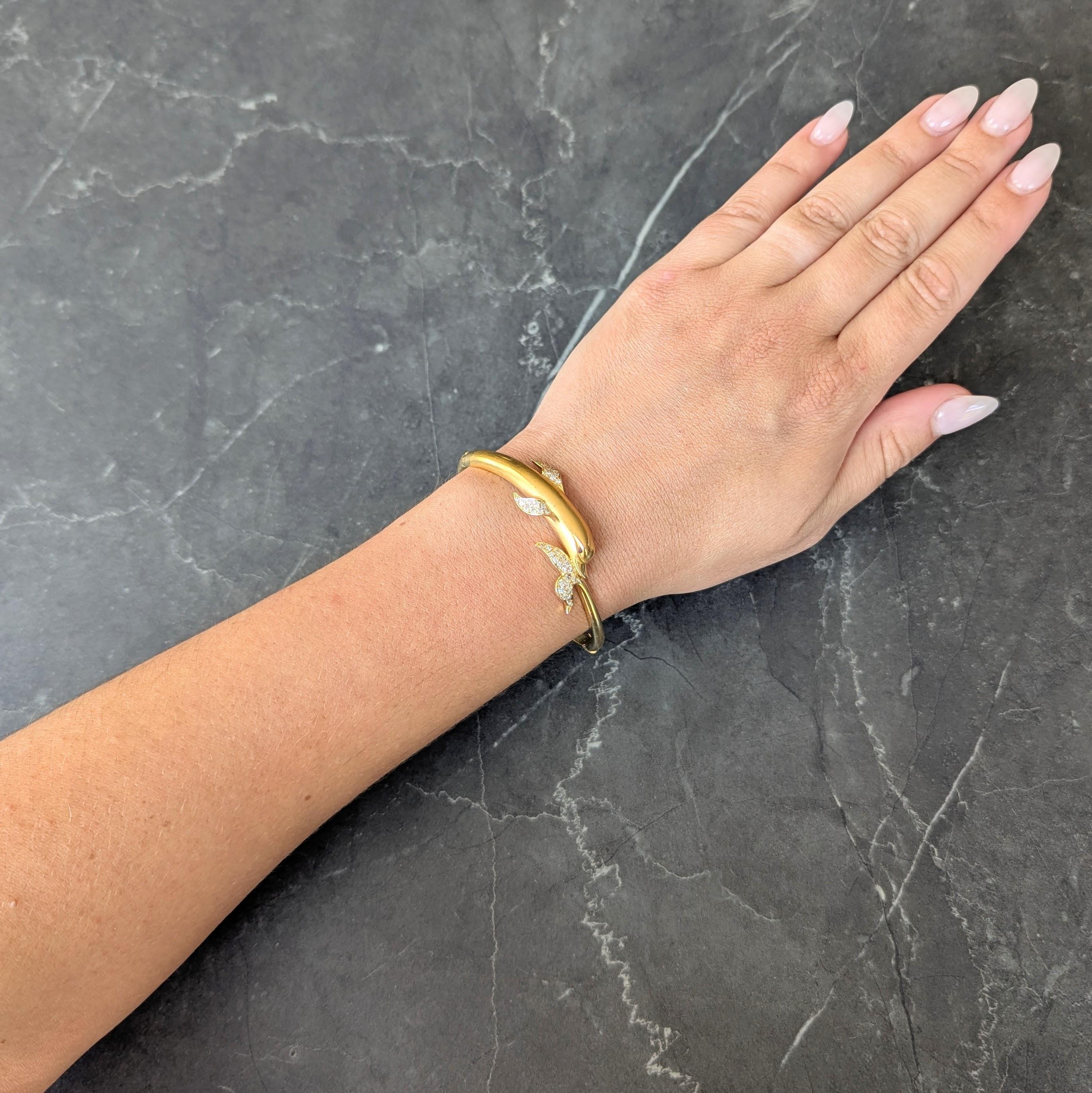 Bracelet de style bypass se terminant par une queue et une tête de dauphin très travaillée.
Avec face matte rainurée et museau et queue hautement polis
Accentué par des diamants ronds de taille brillante sertis à fleur de peau.
D'un poids d'environ