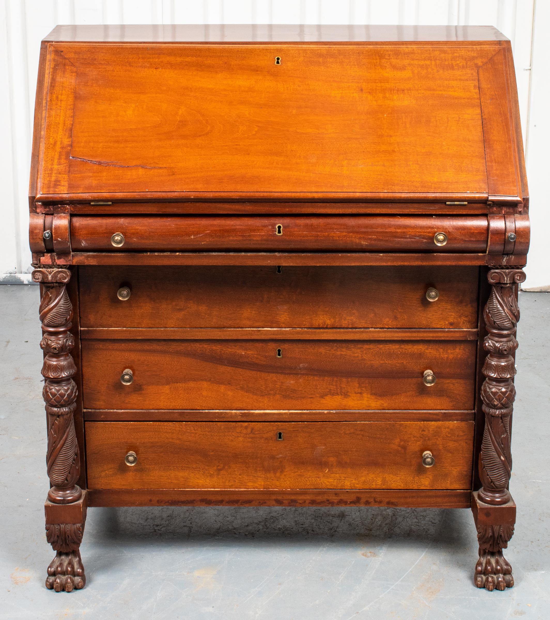 Caribbean Colonial style mahogany slant front secretary, in the late Classical taste, two columns carved with pineapple and palm leaf motifs flanking the three drawers beneath the slant front writing desk. Measures: 41” H x 36” W x 19” D.