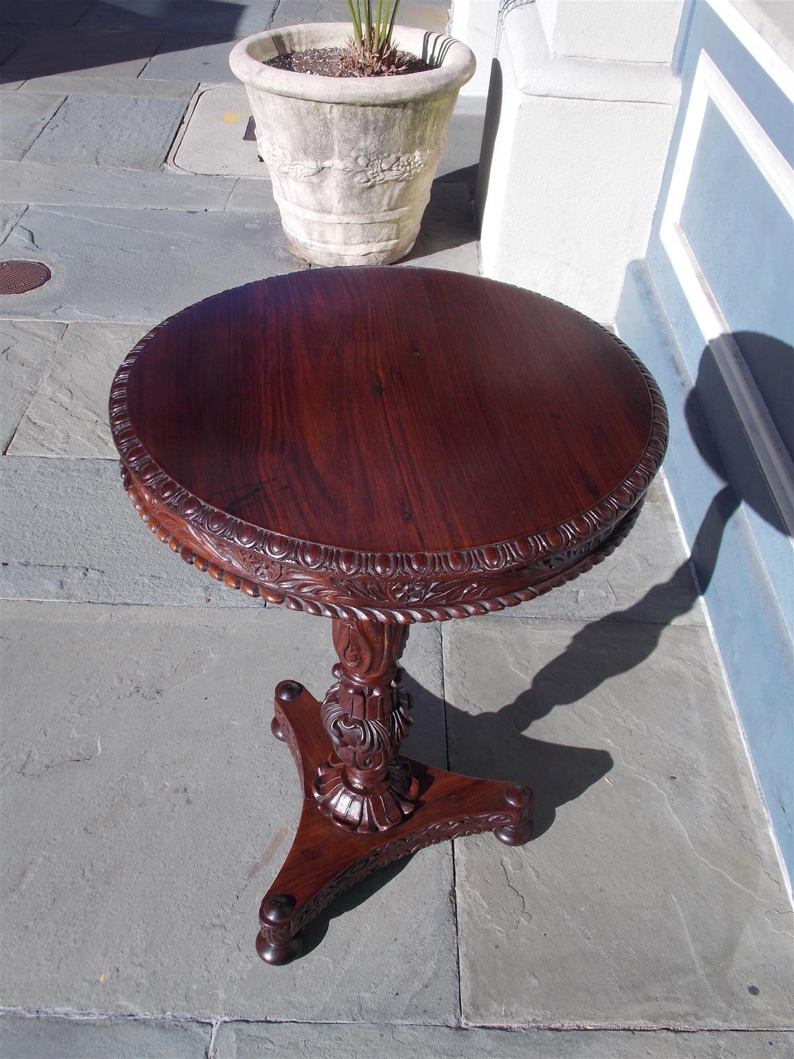 Caribbean mahogany circular tilt top table with acanthus carved foliage, egg and dart border, scrolled acanthus carved medallion frieze, banjo brass locking mechanism, and resting on a tripod acanthus carved pedestal with original bun feet, Early