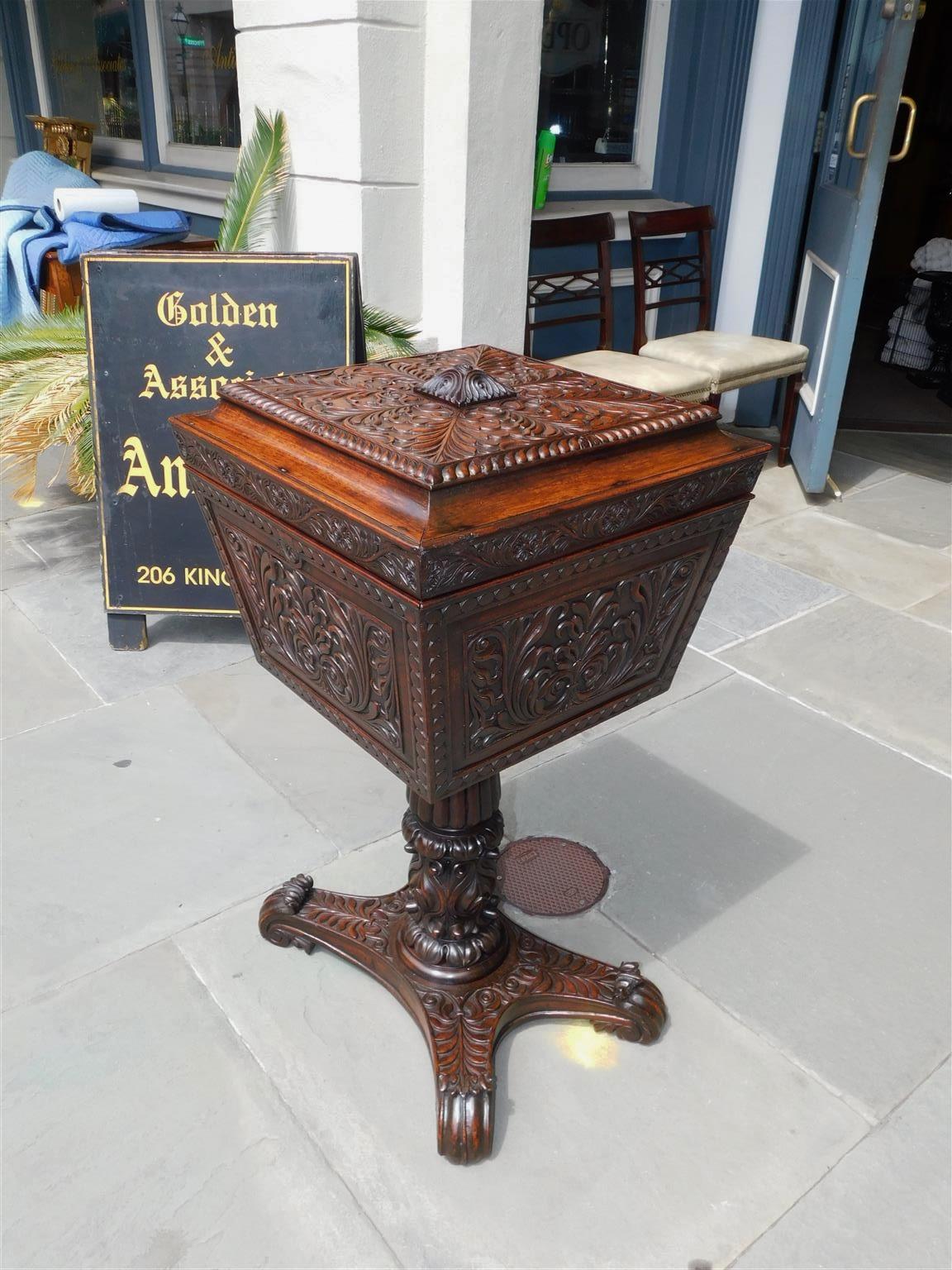 Caribbean mahogany hinged pedestal tea poy with fitted interior, foliate carvings, and resting on the original scrolled feet. Early 19th century.