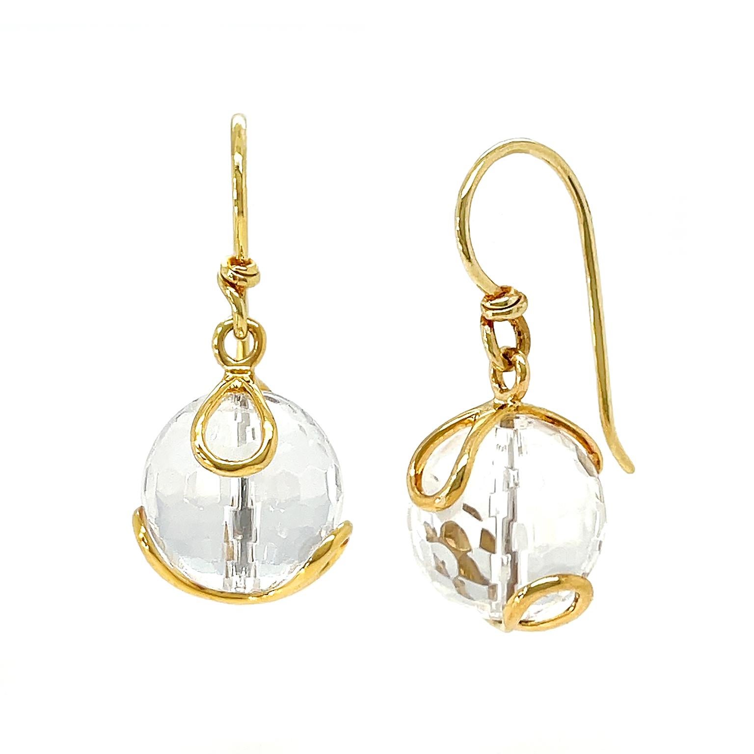 The shimmering translucency of crystal is showcased in these Carina earrings. A facetted globe of crystal produces flickers of light and soft shadows. 18k yellow gold loops secure the gem and French hooks join the ears to the earrings. The total