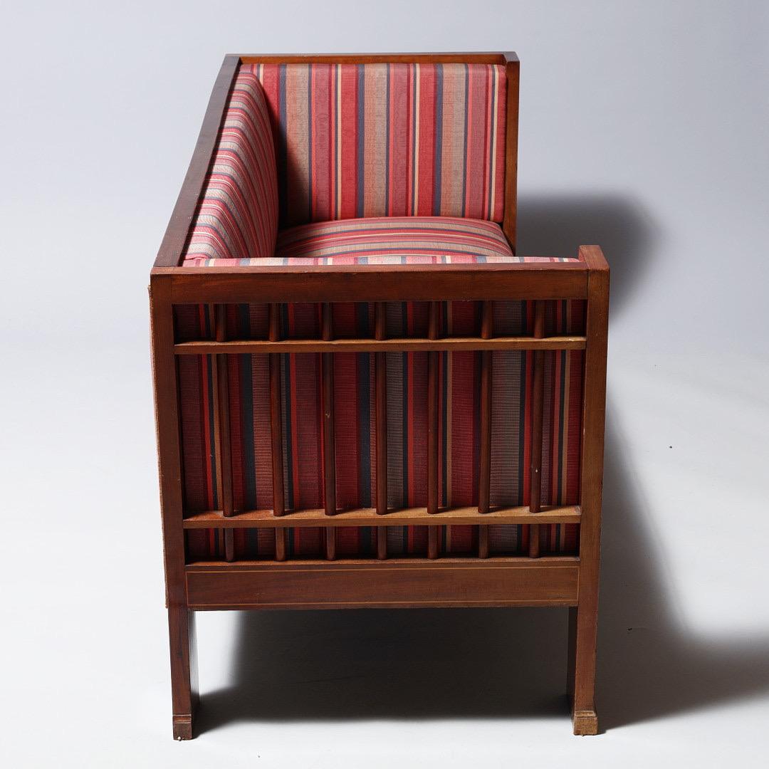 An elegant mahogany sofa crafted by Danish designer Carl Andreassen, who worked under the renowned architect Martin Nyrop. The sofa is decorated with delicate inlays and retains a later striped upholstery fabric, combining historic craftsmanship