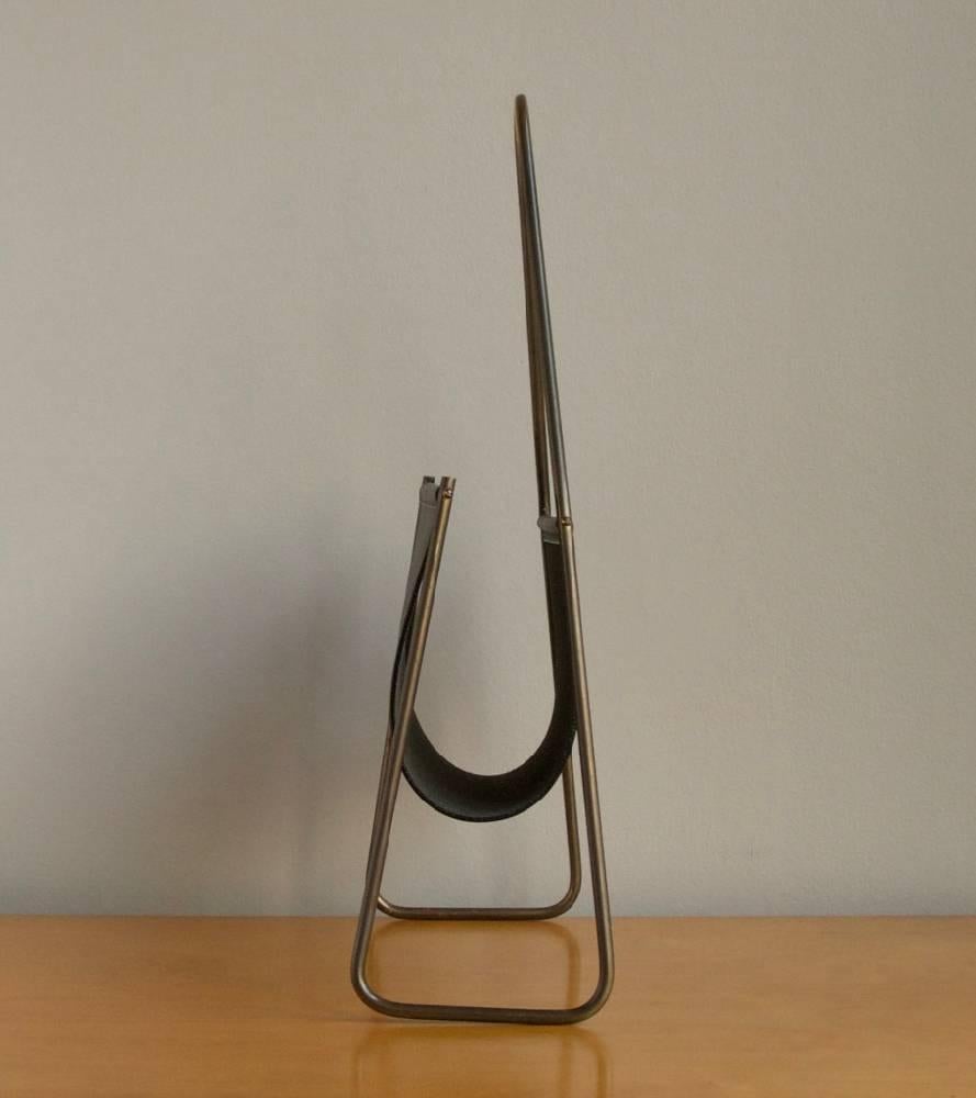 Magazine holder designed and made in the Auböck Werkstatte, Vienna, circa 1960.
Numbered as design 3808 of the Viennese workshop, it features a sinuous frame in polished brass and a leather sling. The brass frame is covered by a uniform patina,