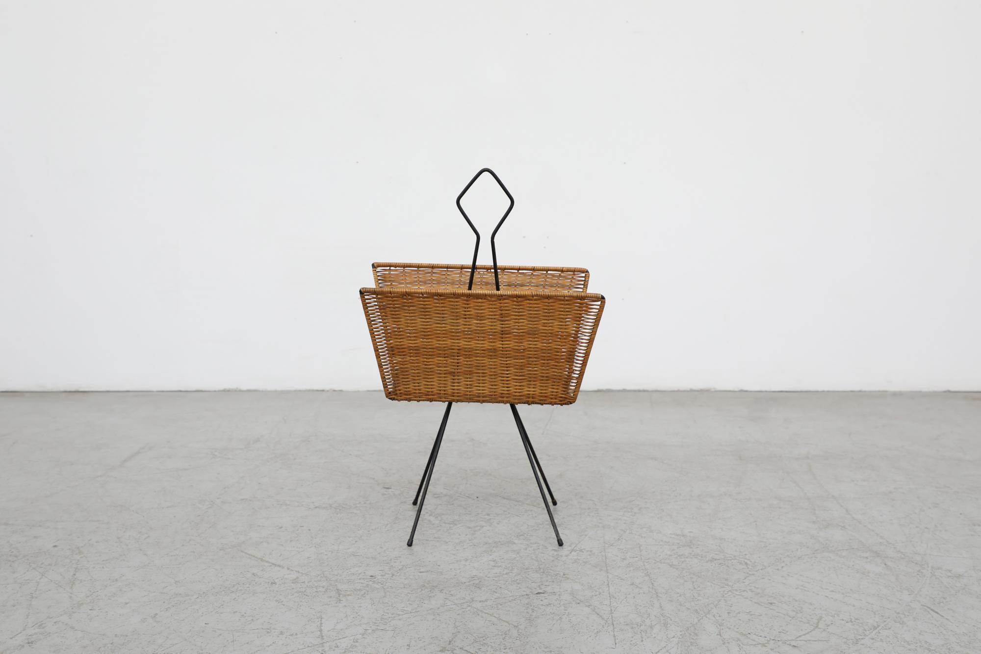 Vintage standing magazine rack with rattan holder and black enameled frame. In the style of Jean Royère. In original condition with visible wear consistent their age and use.