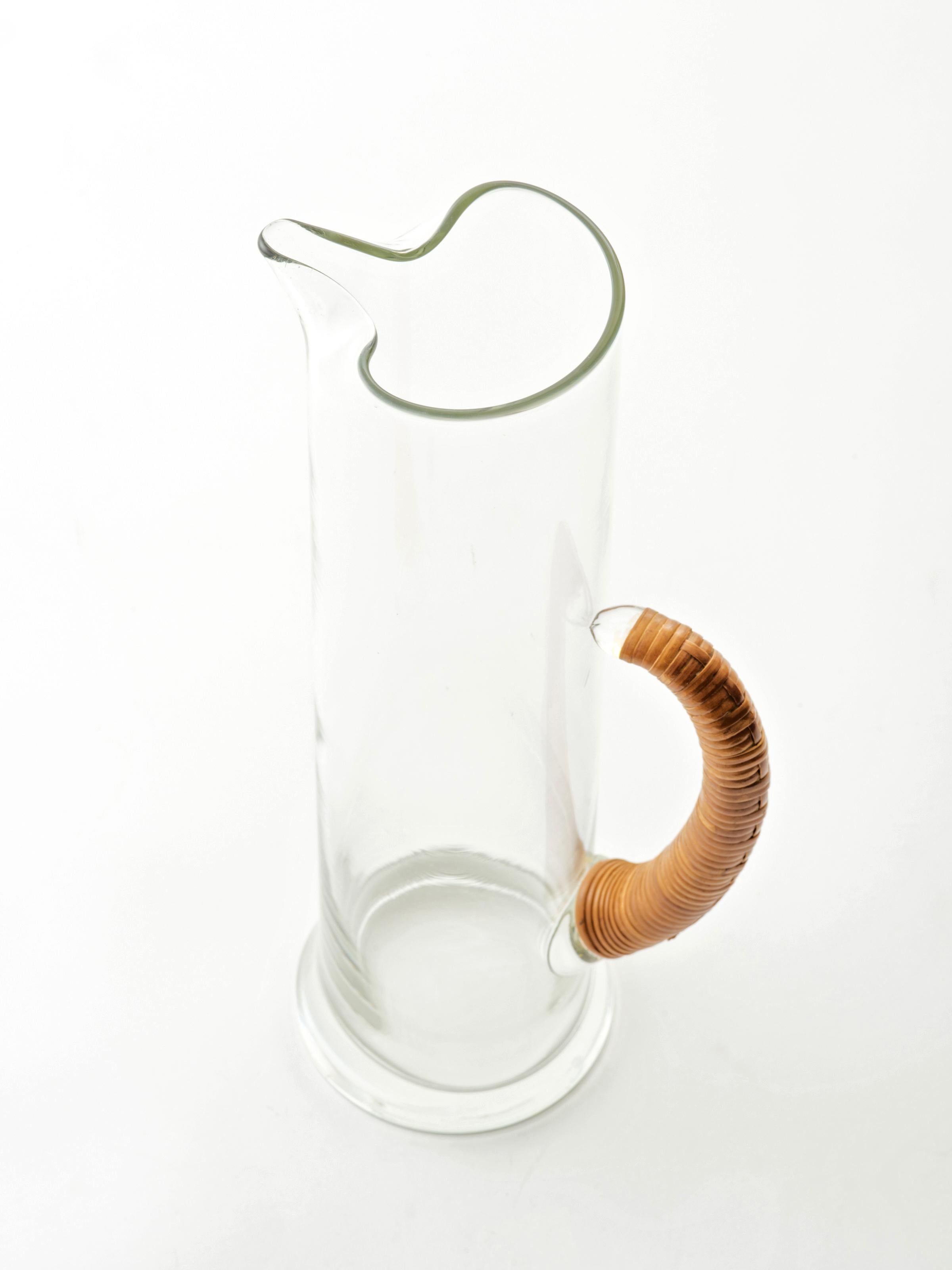 A tall and thin glass pitcher with a cane wrapped handle that's deceptively attached only at the bottom end - - a subtle and elegant design feature. Cane is in great condition with a warm patina.