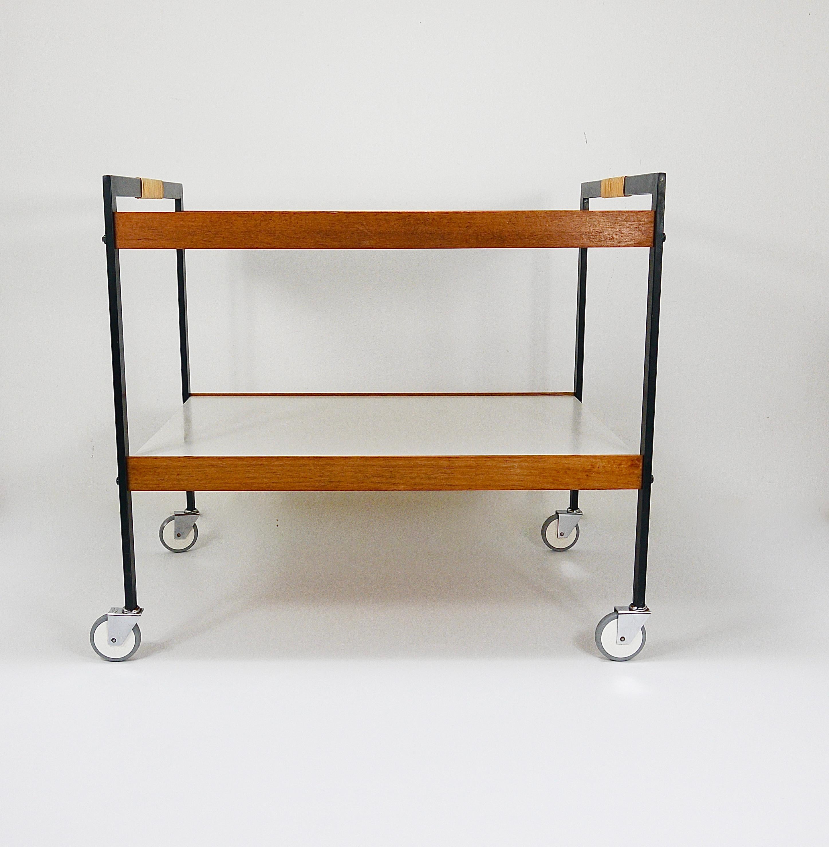 A wonderful example of Minimalist Modernist design, this two-tier bar cart or drinks serving trolley dates back to the 1960s/1970s. Crafted by the workshop Werkstätte Carl Auböck in Vienna, it stands as a beautiful Midcentury piece. The cart