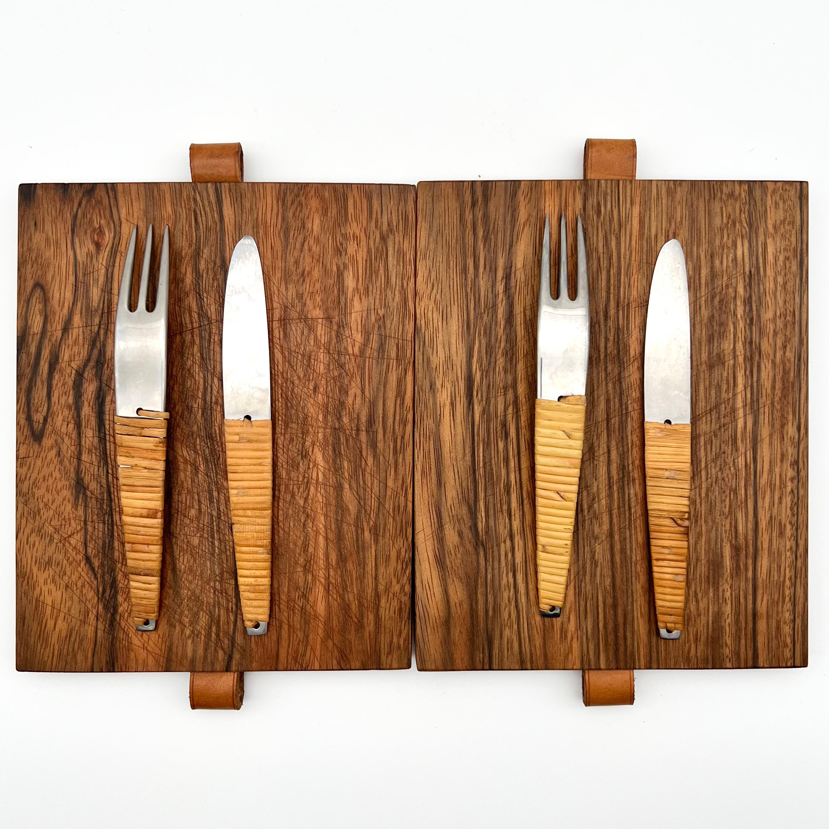 Carl Auböck cutting board & knife and fork set. 
2 sets available 

Original detailing and finishes, walnut cutting board, stainless steel flatware, rattan wrapped handles, leather strap.

Stamped signature to blade: “Auböck stainless made in