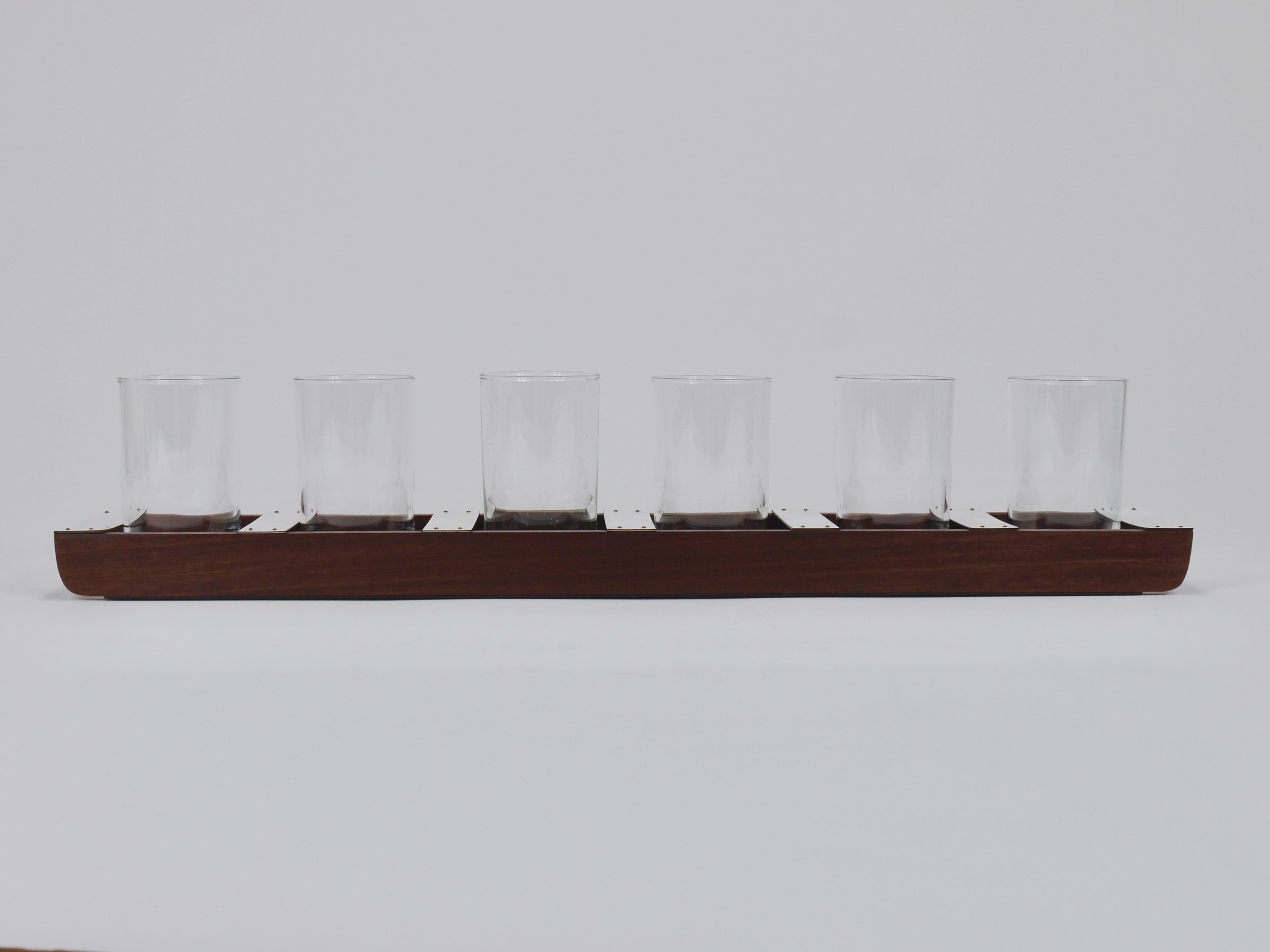 Un vassoio lungo minimalista ed elegante della metà del secolo scorso, con sei bicchieri lunghi trasparenti degli anni Sessanta. Progettato e realizzato da Carl Auböck a Vienna. Il vassoio è realizzato in legno marrone scuro, con chiodi in ottone,