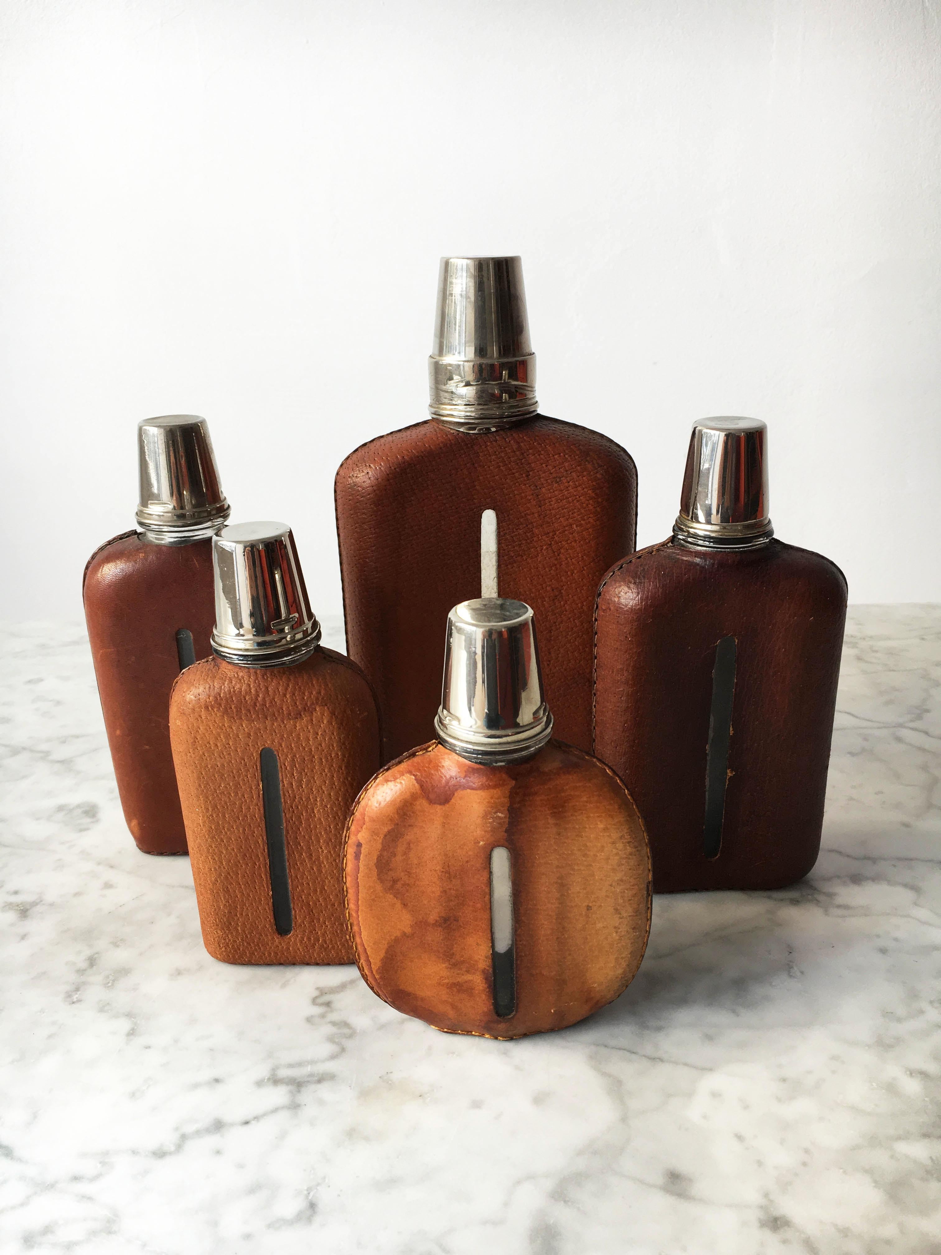 A very rare set of five modernist flasks designed and made in the Werkstätte Carl Auböck. The minimalist sculptural shape is covered in leather, variations in size, from small to extra large. In excellent condition with just the right amount of