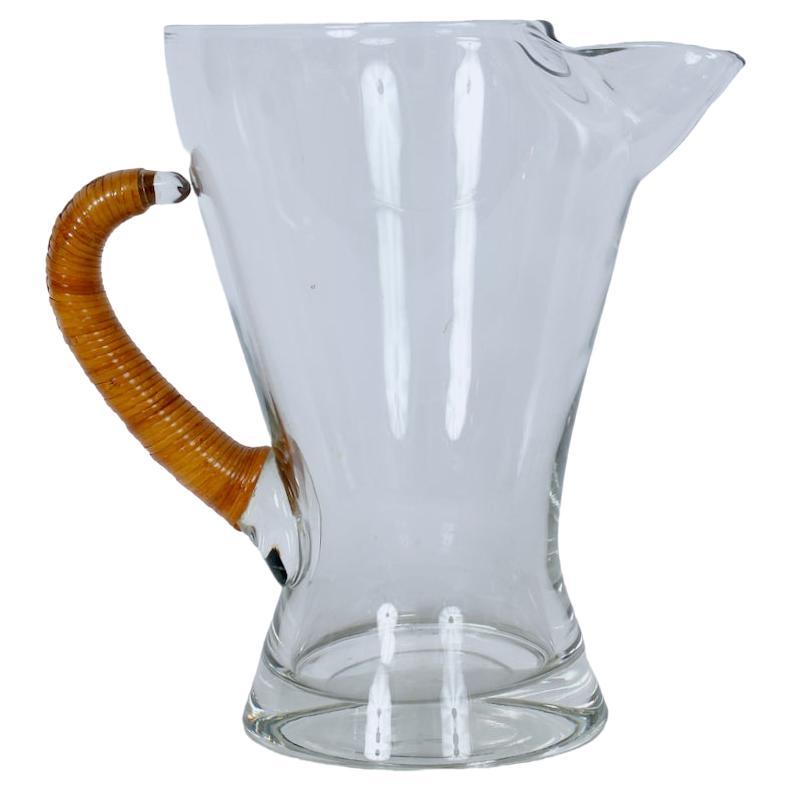 Modern Carl Auböck Glass Pitcher with his classic caned wrapped handle. Featuring a handcrafted large, wide mouth clear Austrian Glass Pitcher with Ice guard, with arched woven cane handle, atop a balanced, circular 4 7/8