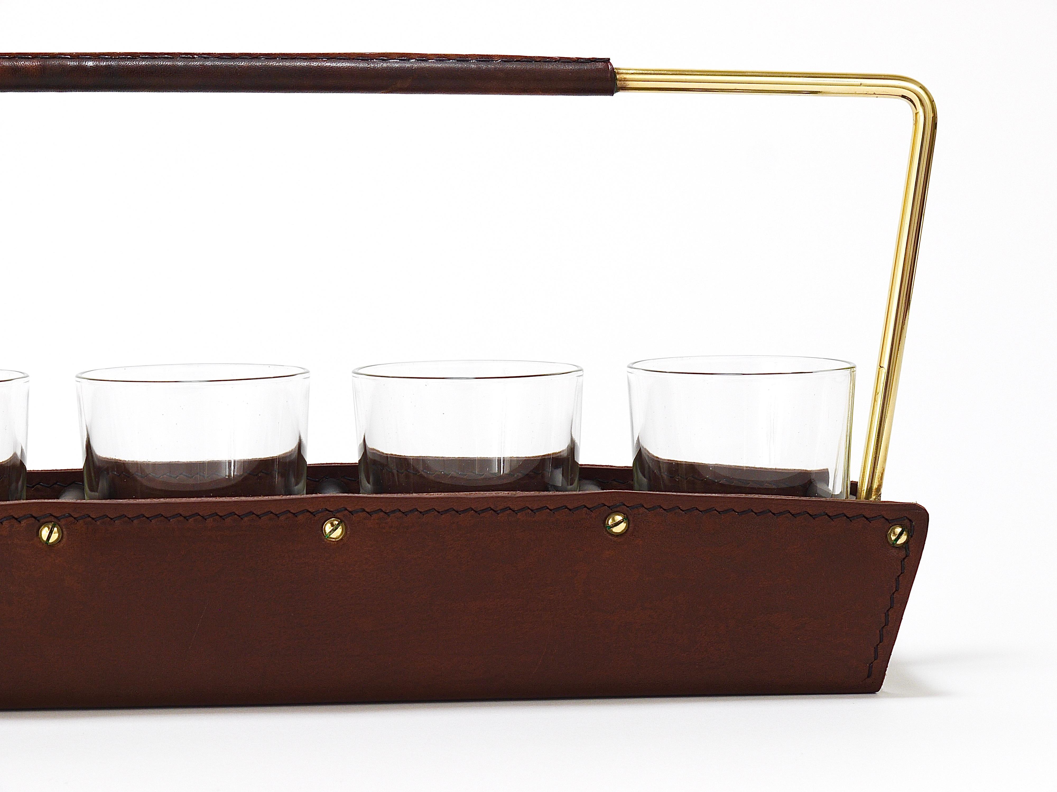 A minimalistic and beautiful midcentury modern long tray drinks carrier / drinking glass caddy with 6 clear glasses from the 1950s. Designed and executed by Carl Aubock II in Vienna. Made of polished brass and thick brown tan leather. In very good