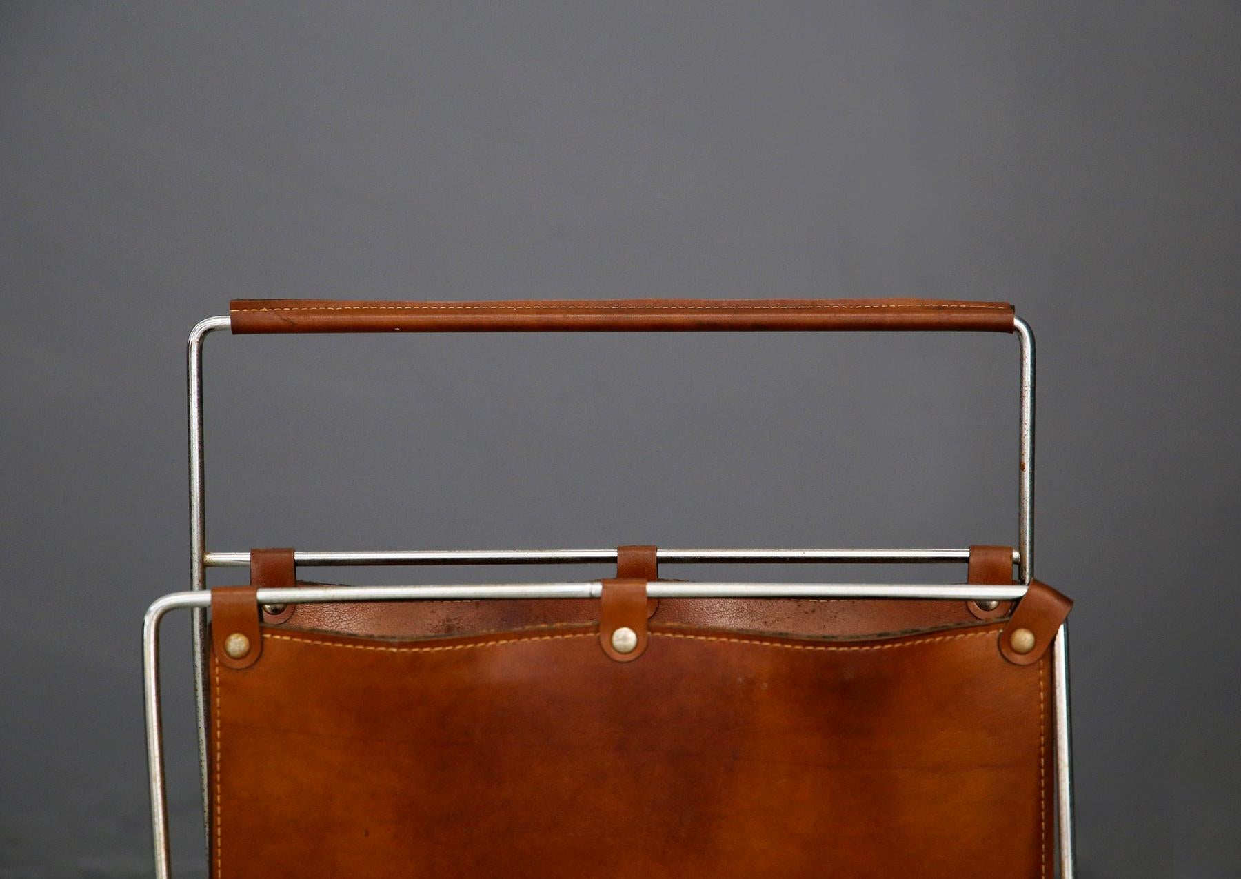 Elegant period magazine rack, Vienna, circa 1950.
Its cladding and handle are made of brown leather with lighter-colored stitching to make them stand out. The frame of the structure is made of nickel-plated steel and covered with a uniform natural