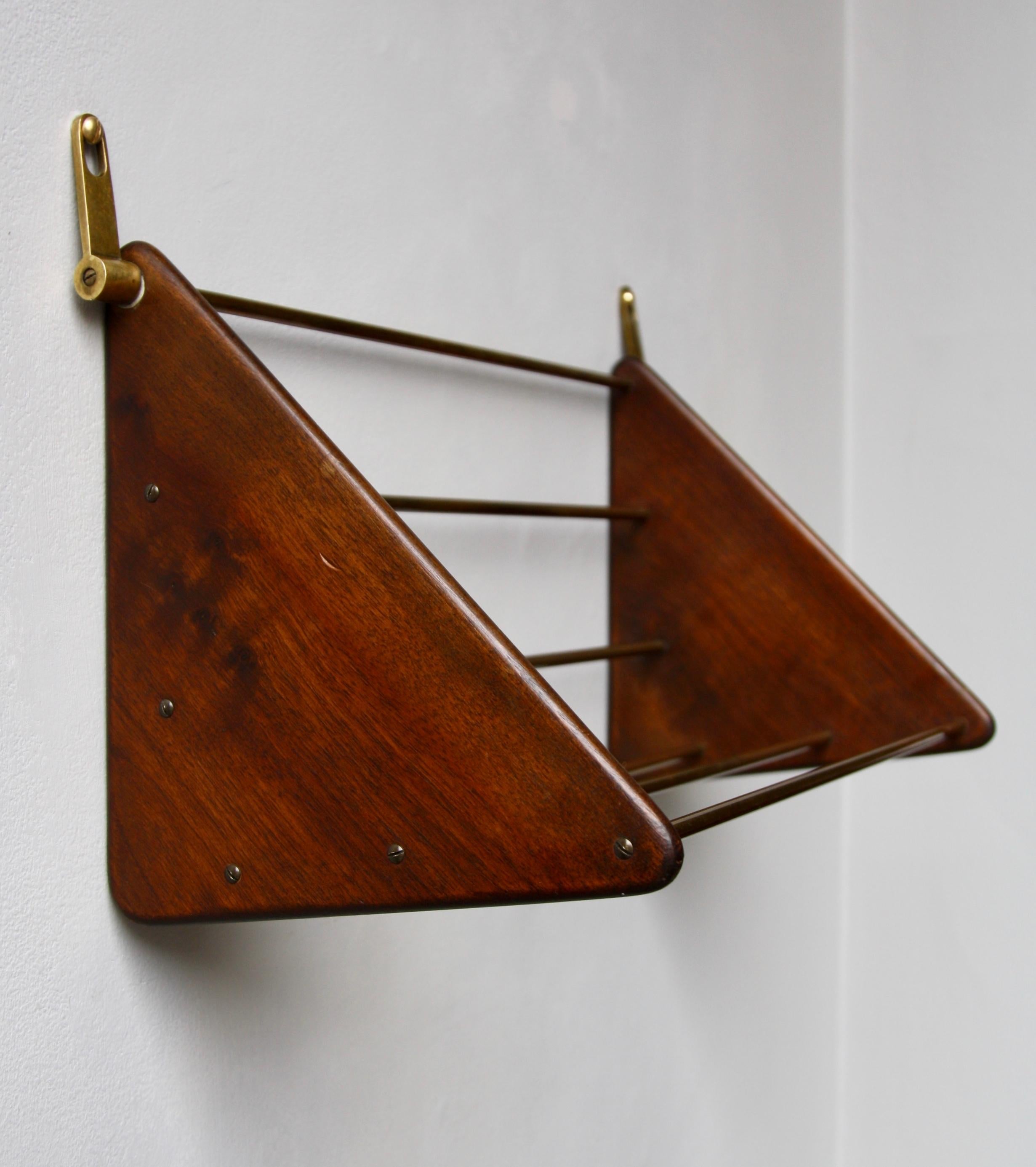 A sculptural shelf designed and made by Carl Auböck II, Vienna, circa 1950. The piece is made up of six horizontal brass bars which connect two walnut triangles whose vertices hang on the wall via two brass hooks, one of them bears the Auböck