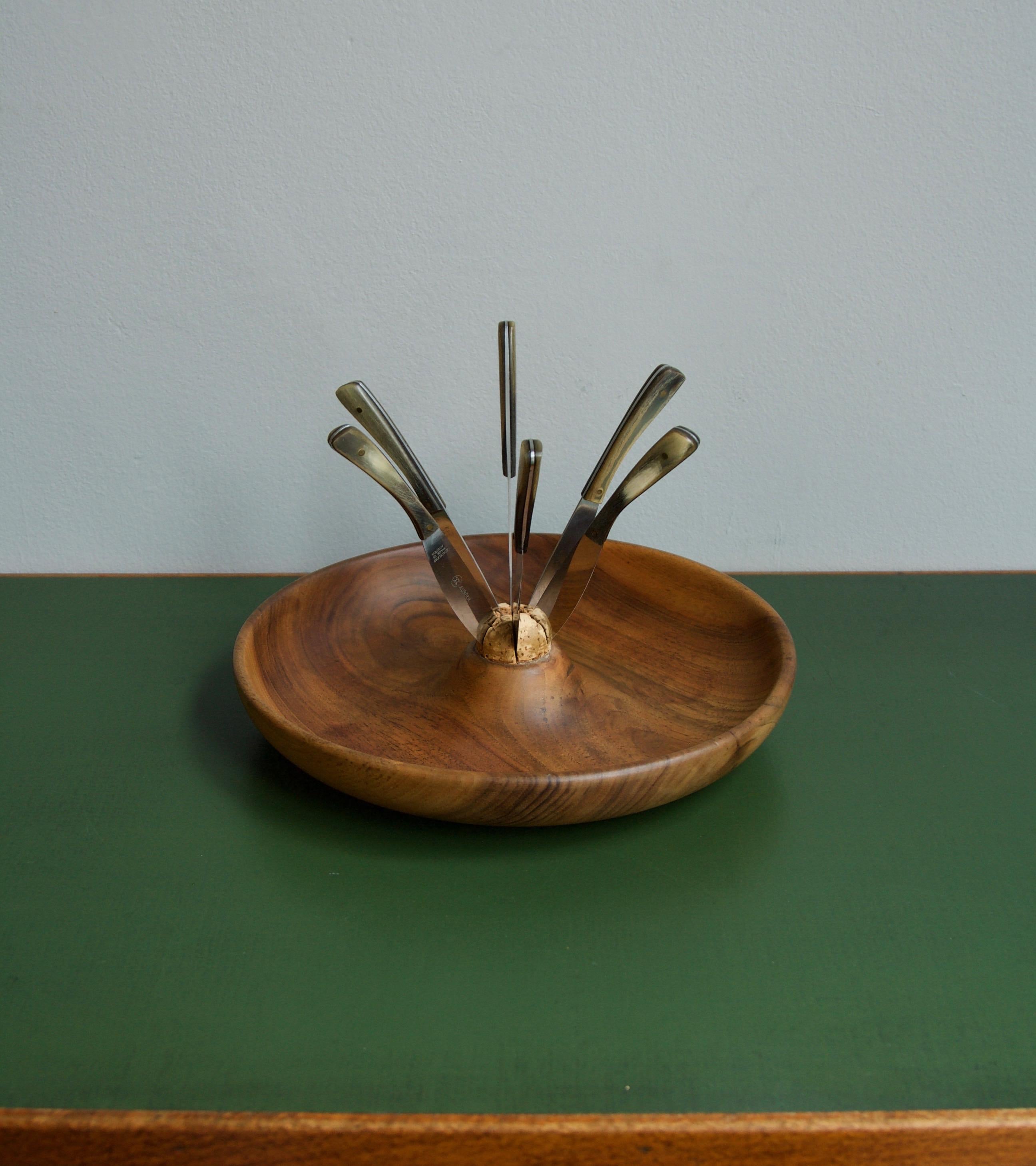 A sculptural fruit bowl and knife set designed and made by Carl Auböck II, Austria, circa 1955.
Formally known as Model #4640 the set consists of a carved walnut wood bowl with a cork insert and a set of six stainless steel knives with horn clad