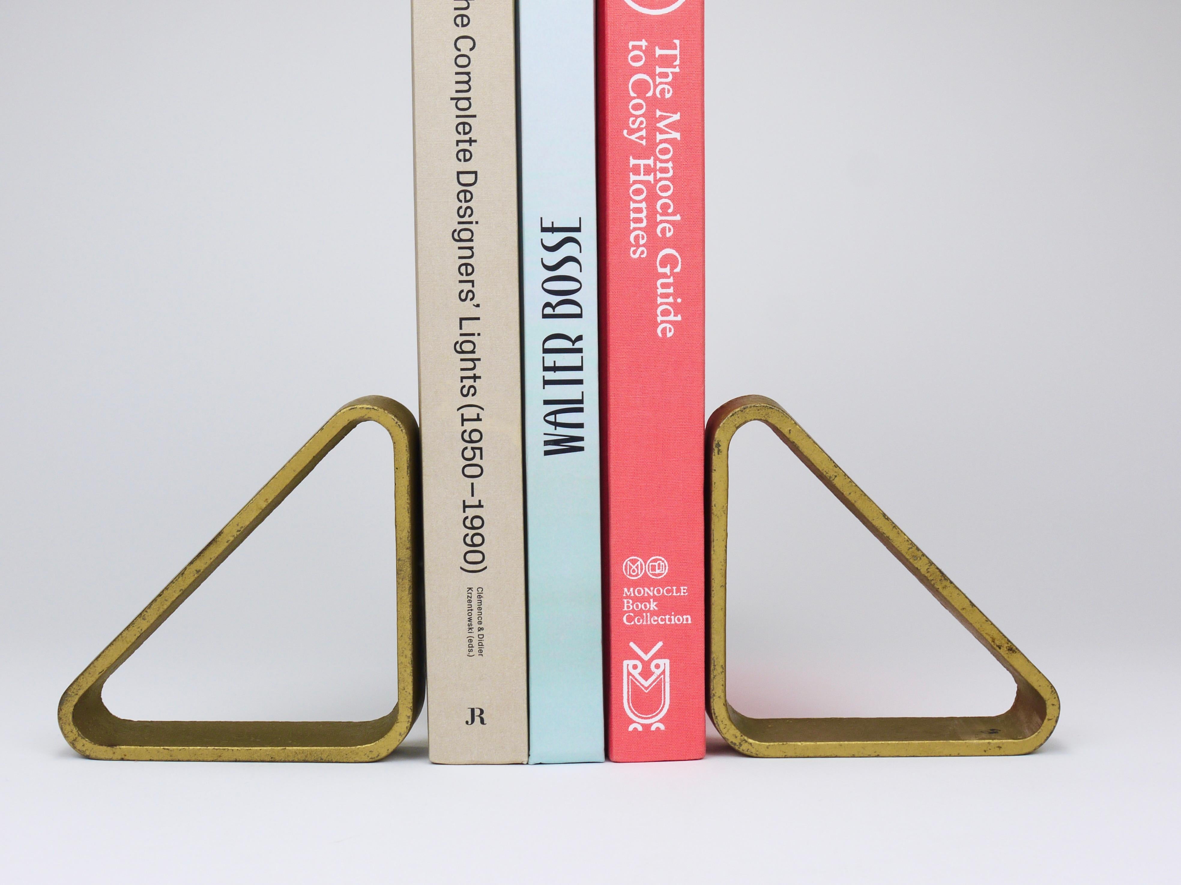 Paire de serre-livres triangulaires en métal des années 1970, modèle 5443, conçus et fabriqués par Carl Auböck III dans l'atelier Carl Auböck Werkstätte. Elles sont fabriquées en fonte massive avec une finition dorée. Les serre-livres sont en bon