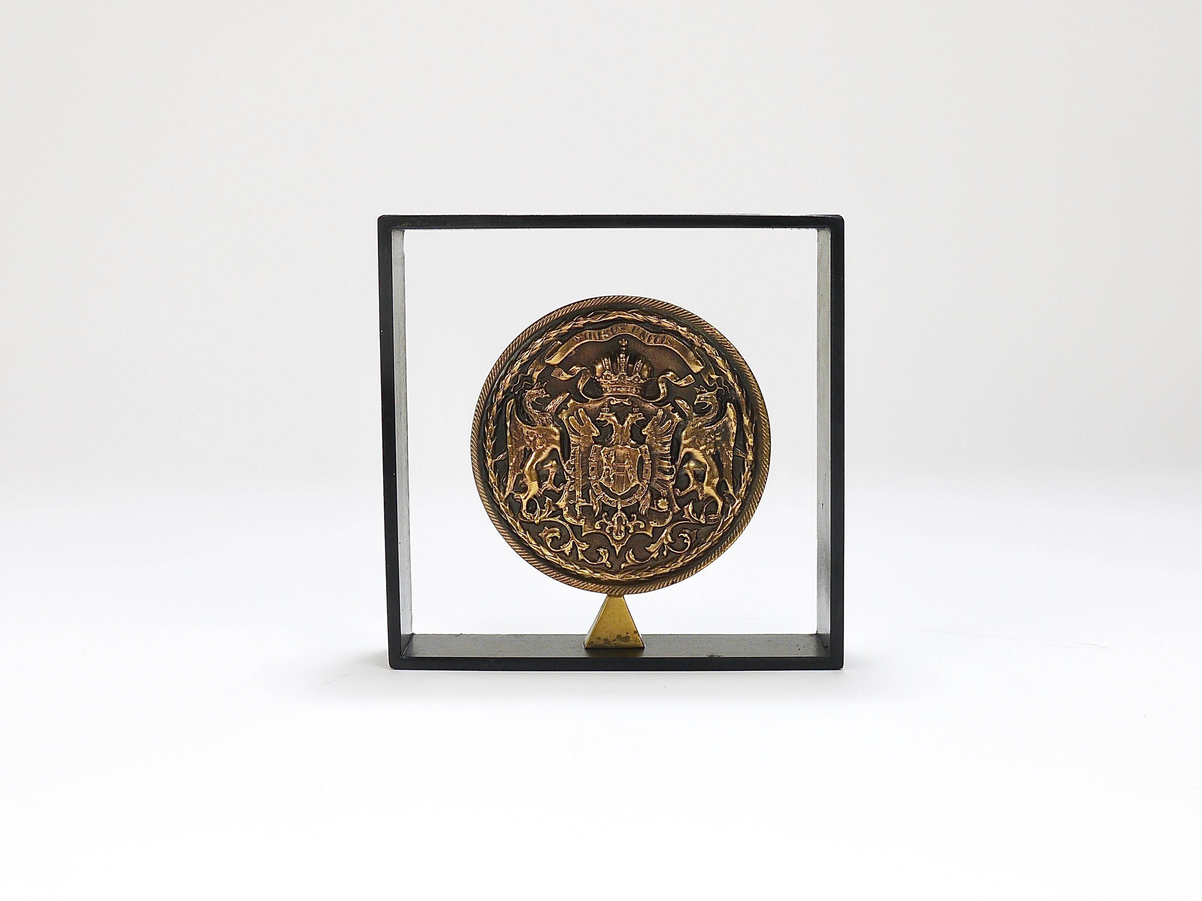 This is a rare modernist book end, designed and manufactured by Carl Auböck III in the 1970s. The bookend consists of a large brass medal, which displays the coat of arms of the house of Habsburgs, the double headed monarchy eagle and the words