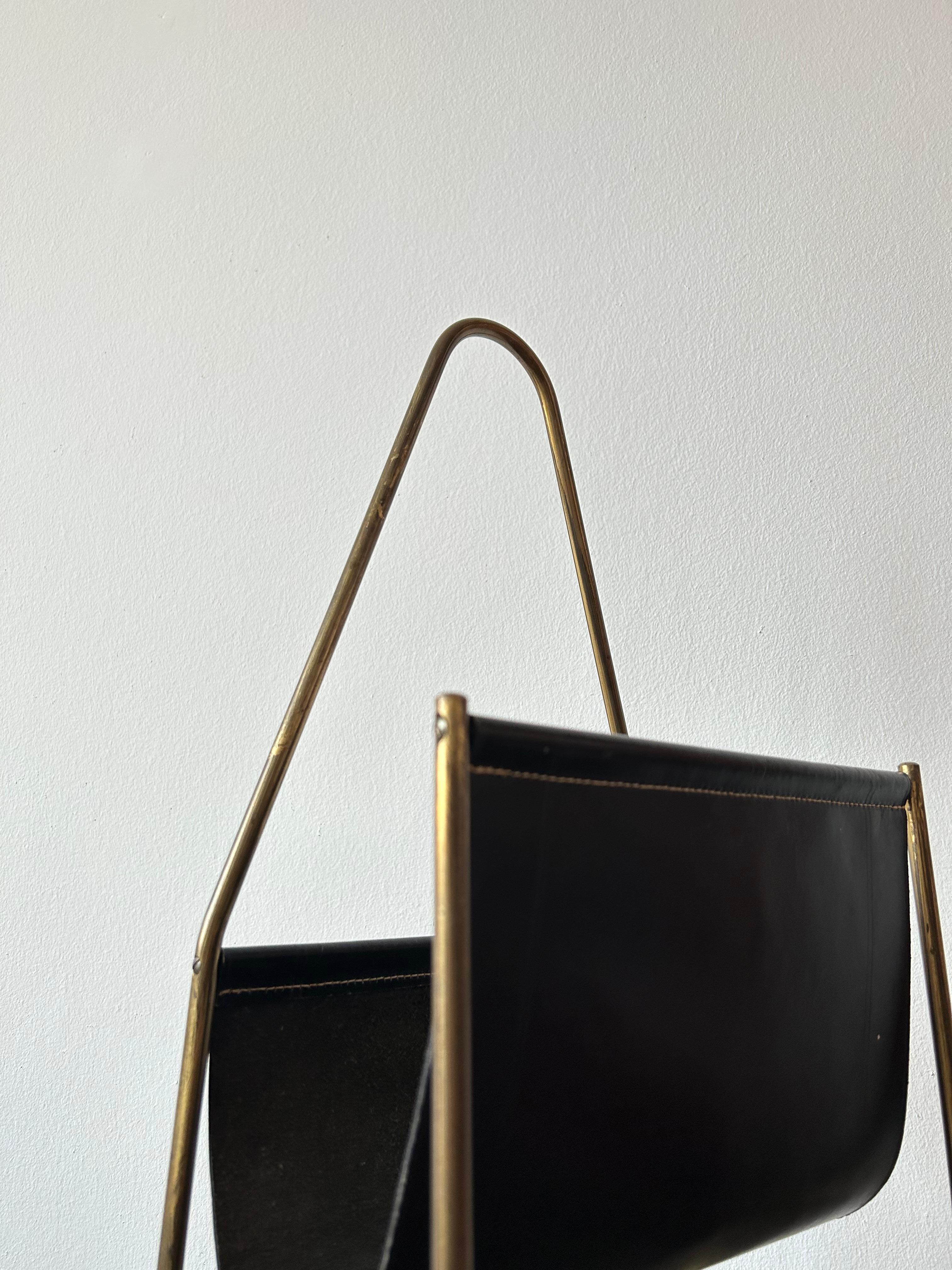 Magazine holder by Austrian designer Carl Auböck in patinaed brass and thick black leather which only will get more charming over the years.

The magazine holder is in good condition and the perfect detail to any interior and will fit all