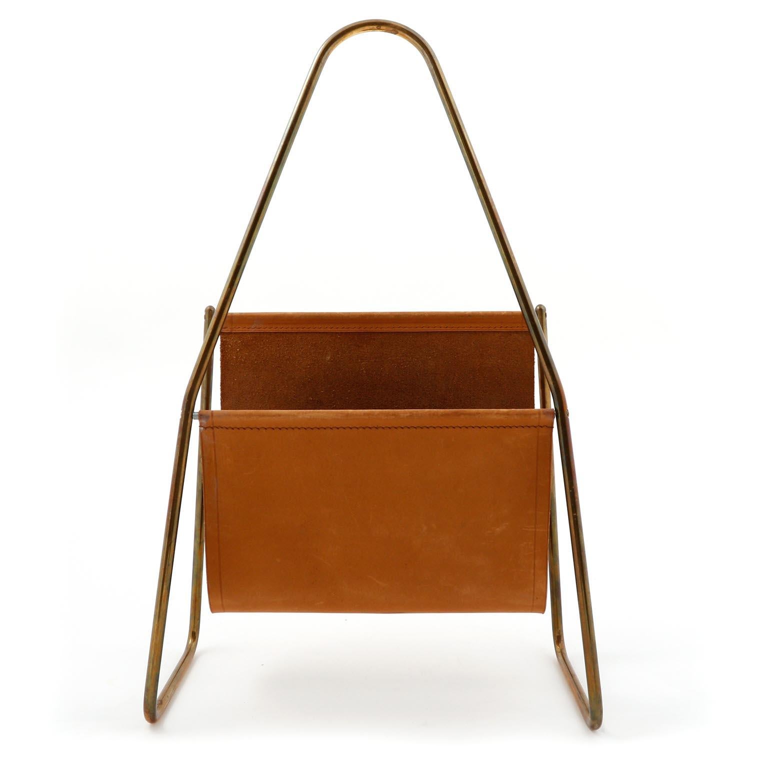 A magazine or newspaper tray made of patined brass and cognac or light brown leather designed by Carl Auböck, manufactured by Carl Auböck workshop in midcentury, circa 1950, Vienna, 1950s. 
An authentic handmade piece in very good original